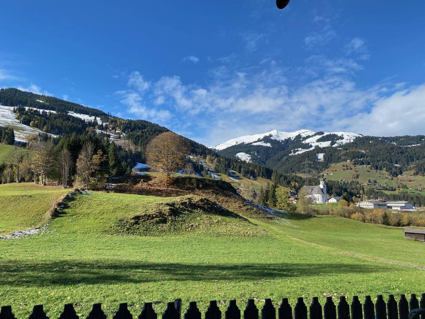 Beeindruckende Bergkulisse mit grünen Wiesen, Wäldern und einem Dorf in der Ferne.