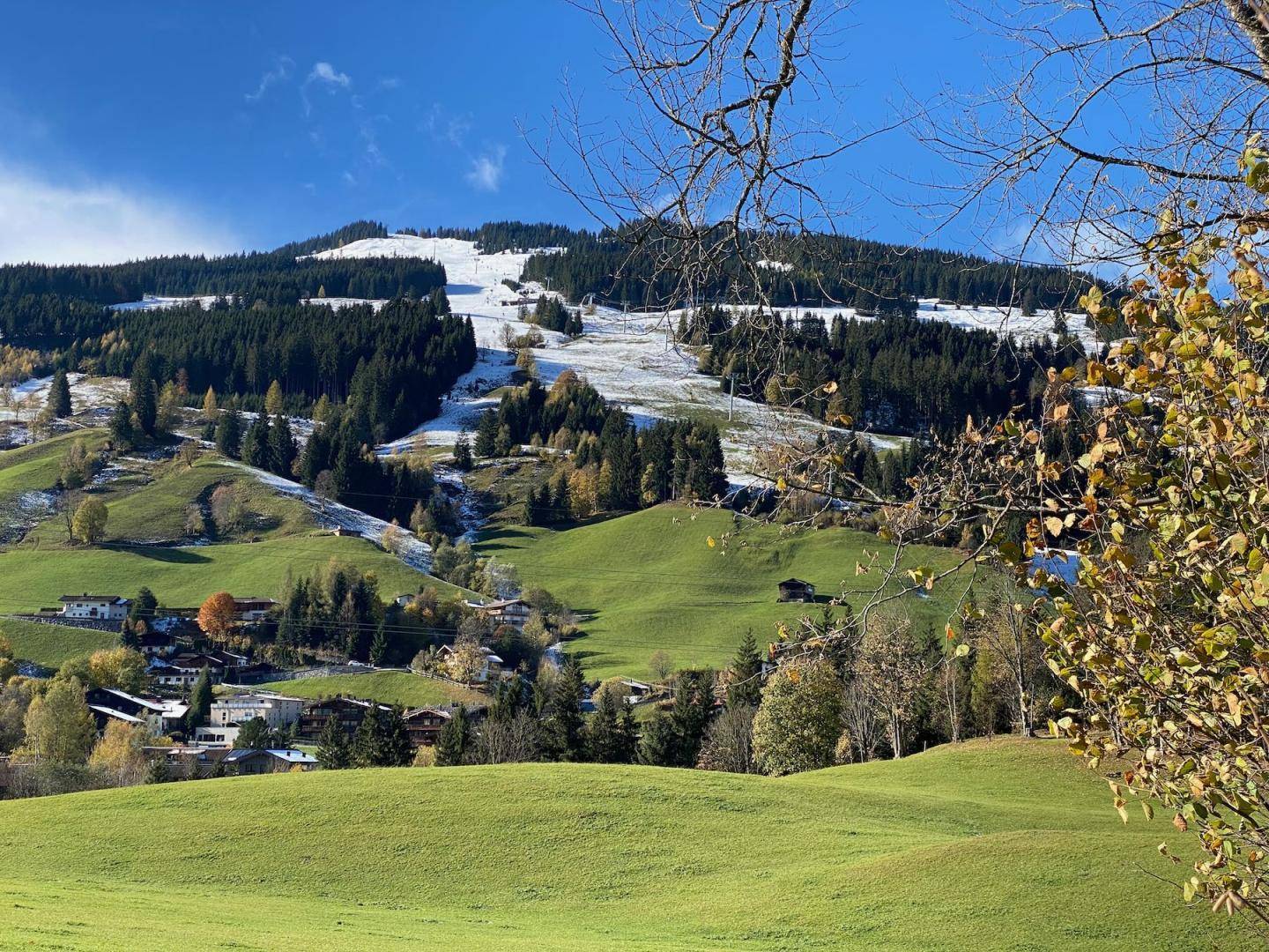 Panoramablick auf die alpine Landschaft mit grünen Tälern und schneebedeckten Bergen im Herbst.