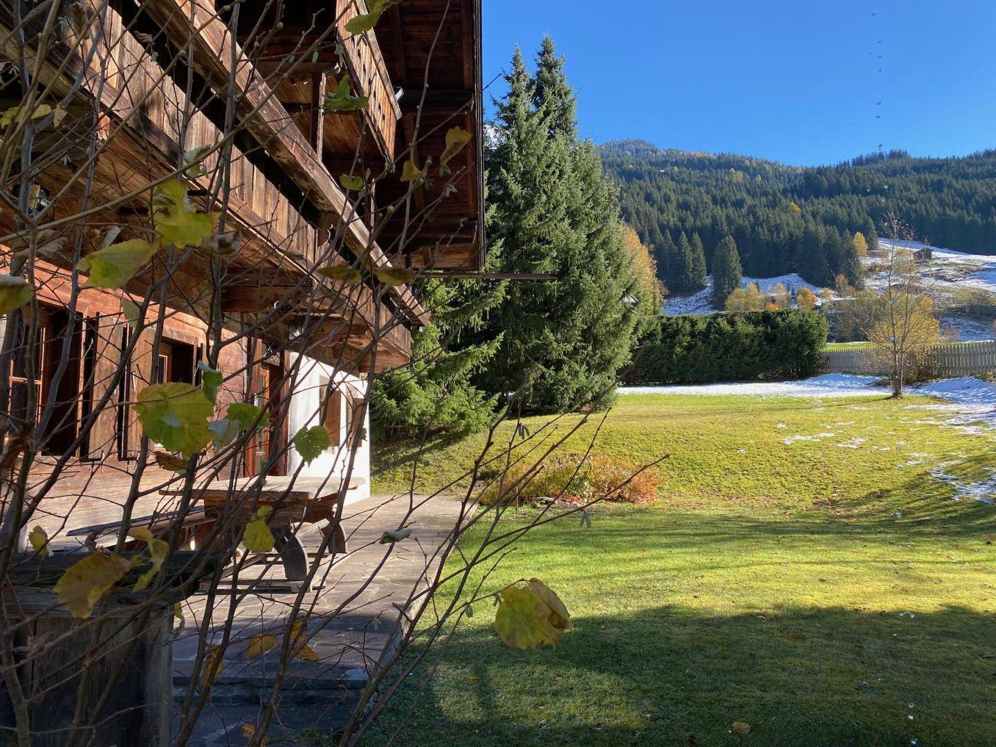 Sonniger Gartenbereich neben dem Haus mit grüner Wiese und Blick auf die umliegende Natur.