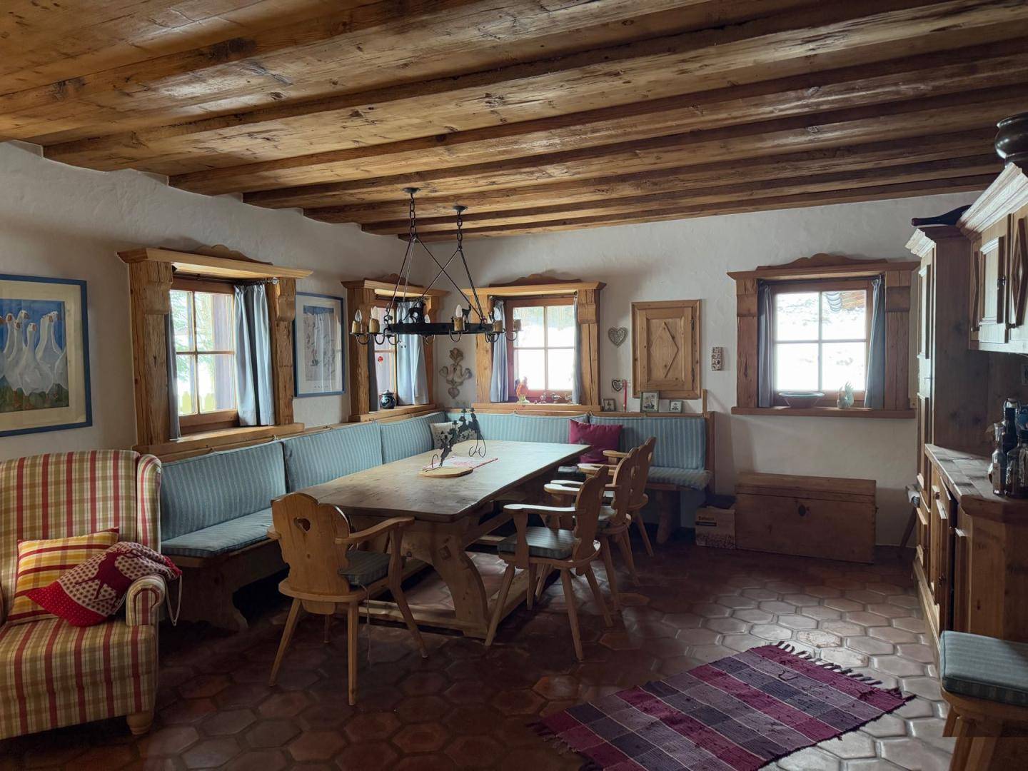 Rustikaler Essbereich mit großem Holztisch, Eckbank und sichtbaren Deckenbalken im Landhausstil.