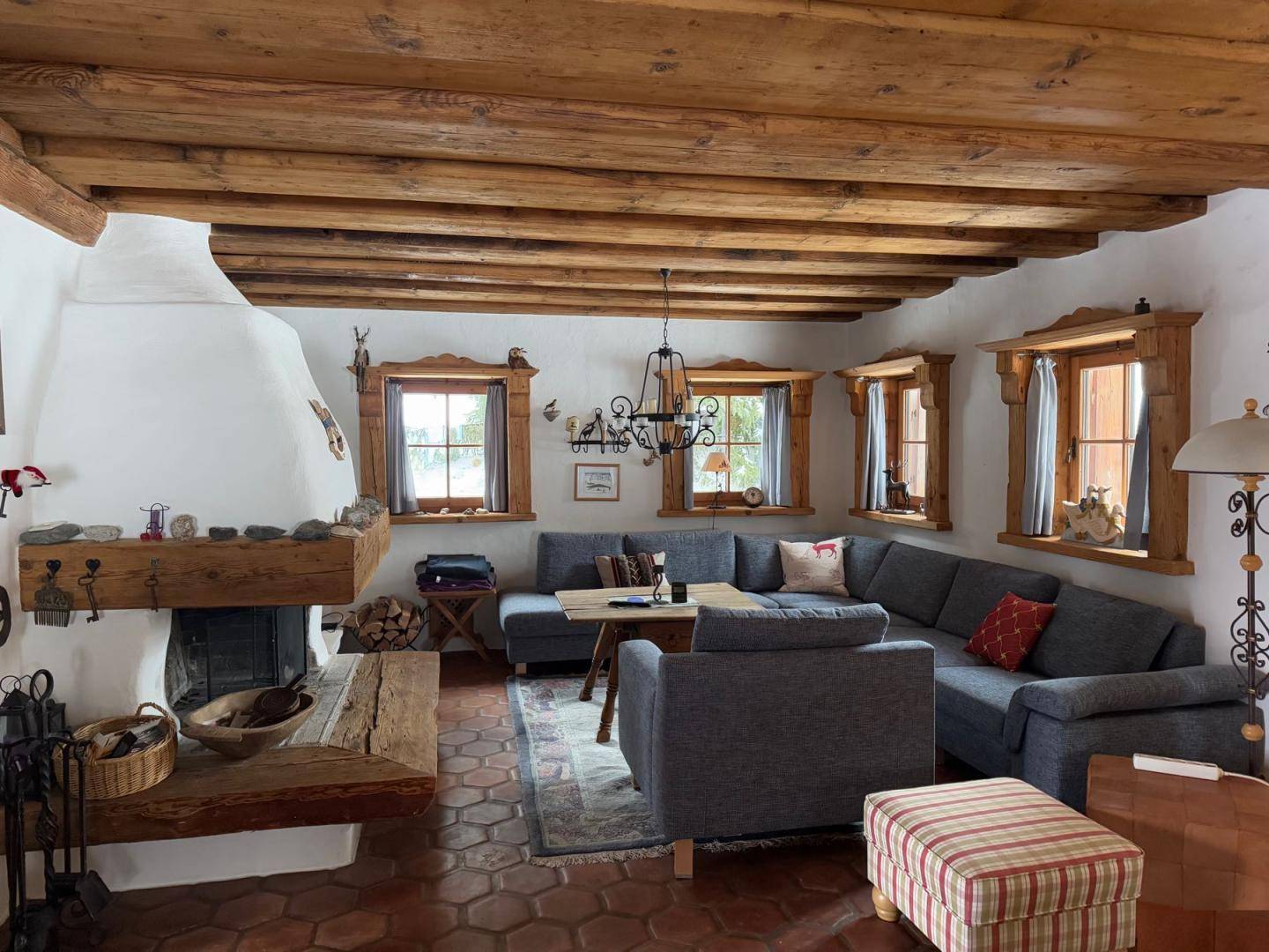 Gemütliches Wohnzimmer im alpinen Stil mit Kamin, Holzbalkendecke und Terrakottaboden.