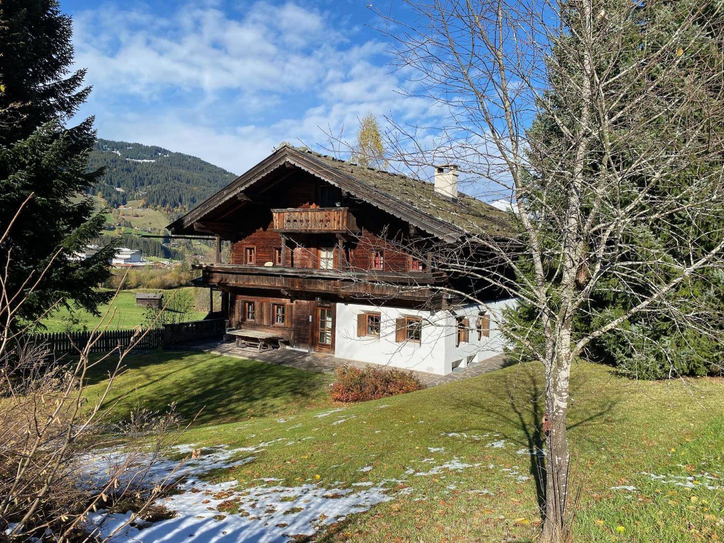 Charmantes Holzhaus mit weiß getünchtem Sockel und alpiner Umgebung unter blauem Himmel.