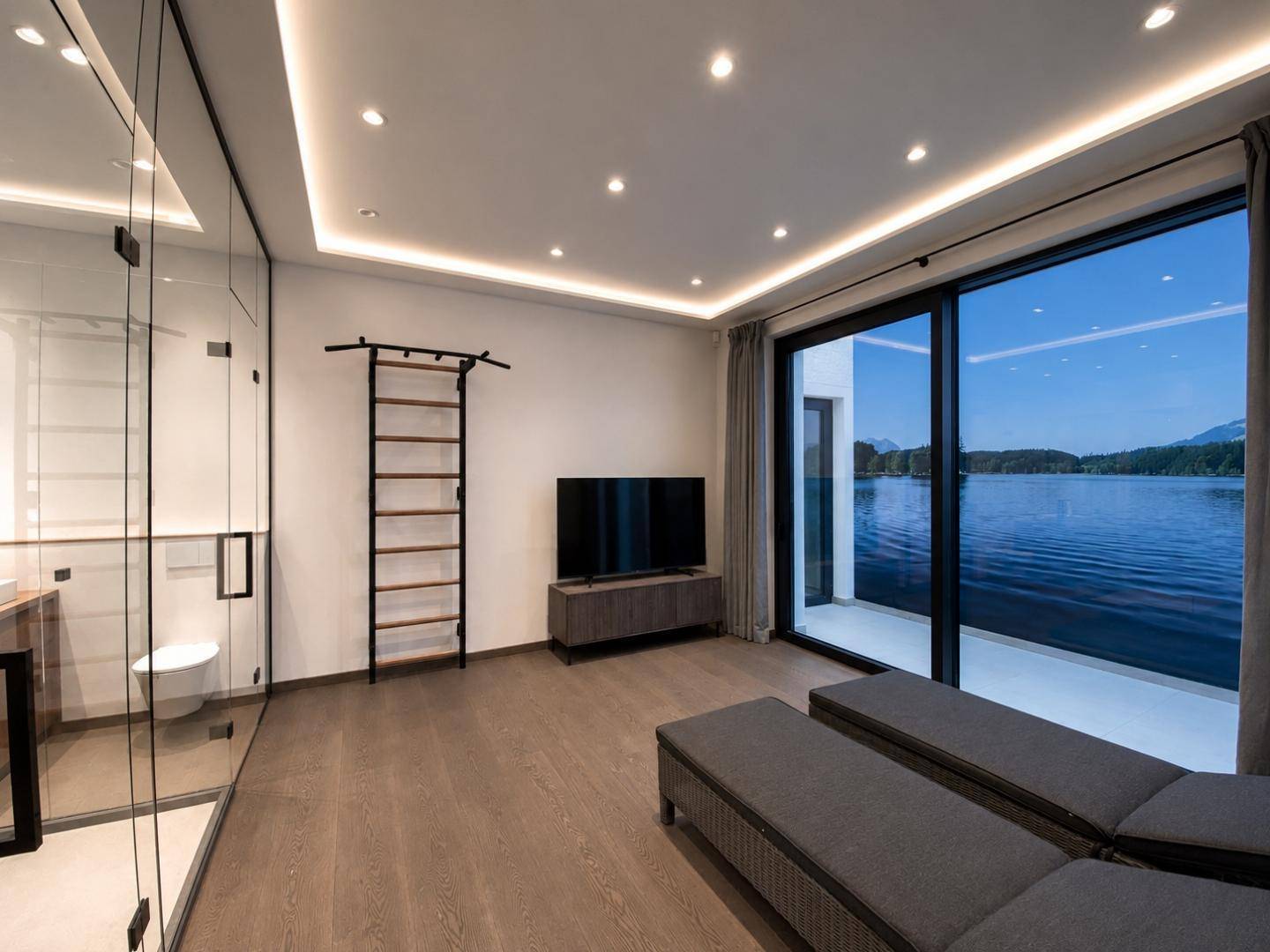 Moderner Raum mit Seeblick, Liegestühlen und integriertem Badezimmerbereich hinter Glas.