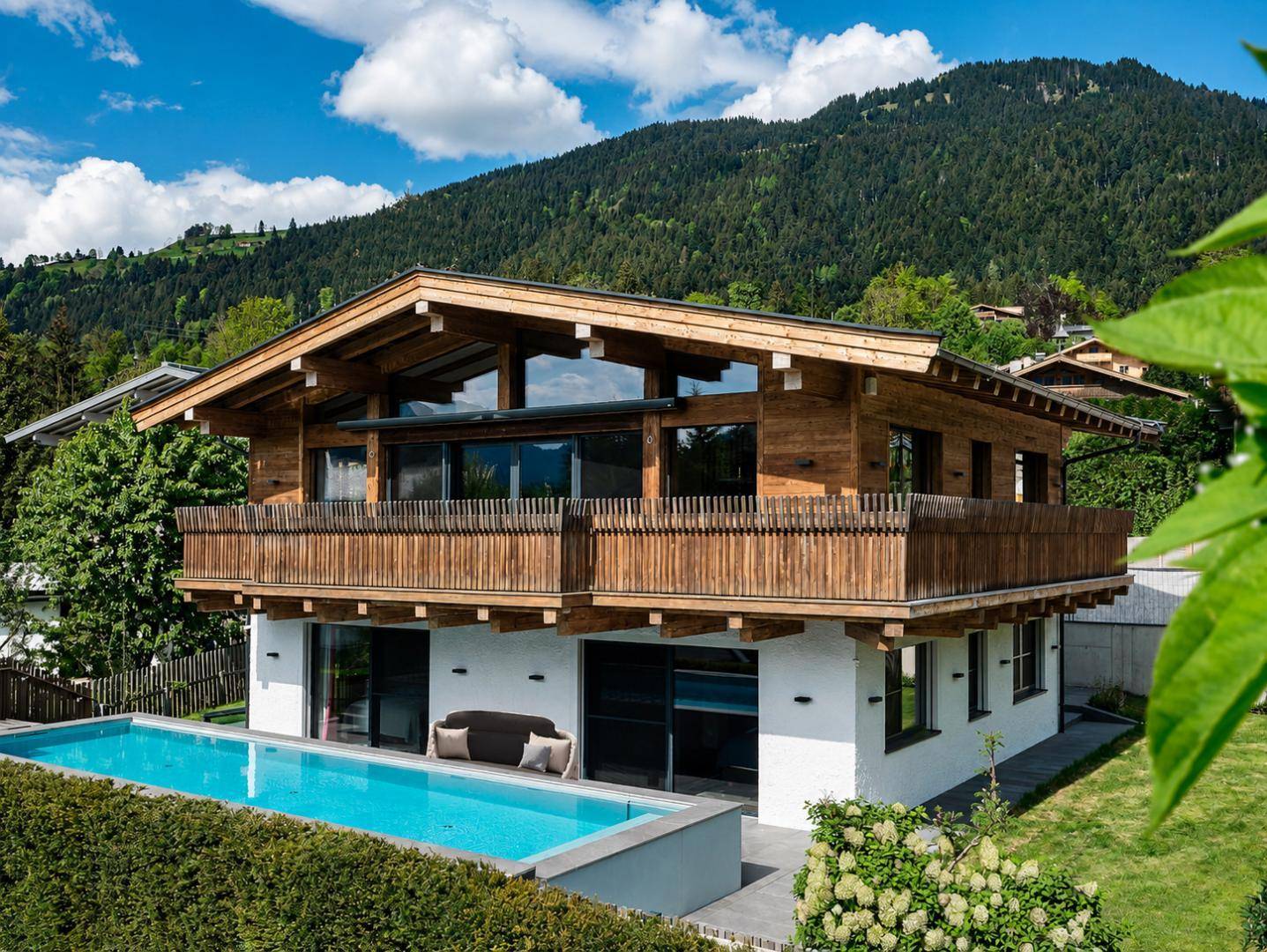 Modernes Chalet mit Infinity-Pool und Bergblick unter blauem Himmel an einem sonnigen Tag.