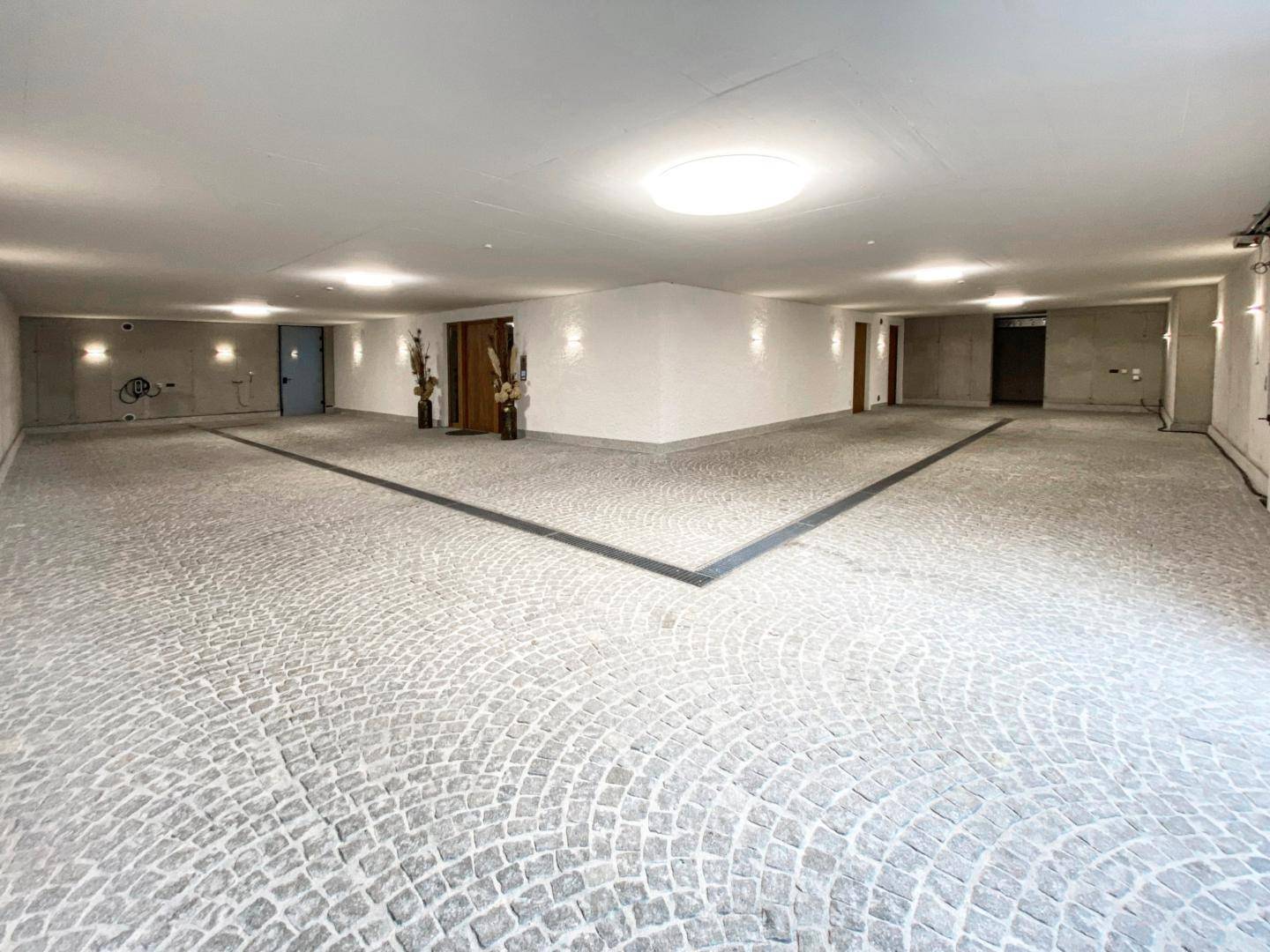 Geräumige Tiefgarage mit Kopfsteinpflasterboden und indirekter Beleuchtung.