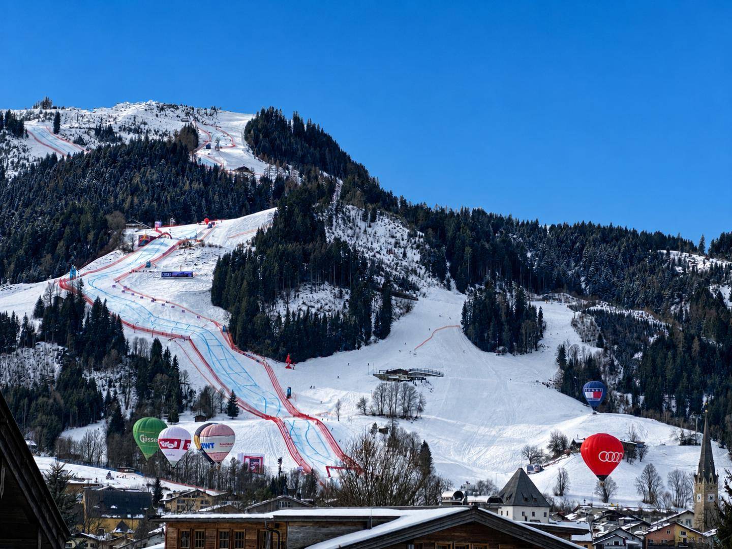 Winterliche Berglandschaft mit Skipisten, Heißluftballons und verschneiten Gipfeln.