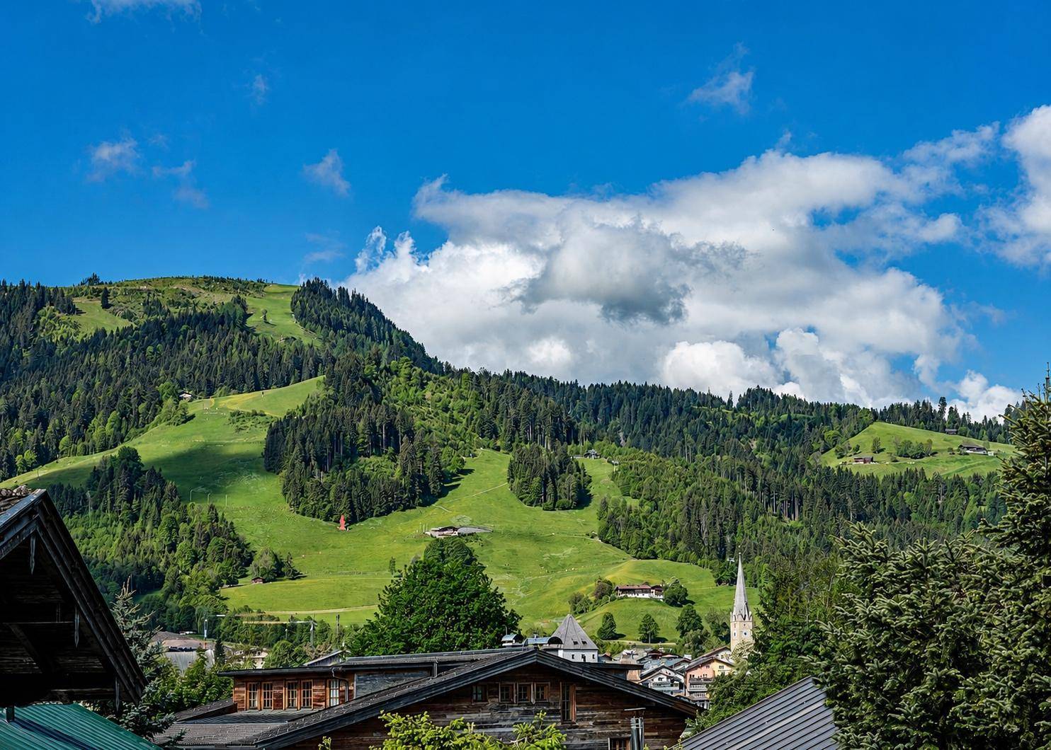 Malerische Berglandschaft mit grünen Hängen, Wäldern und traditionellen Häusern unter blauem Himmel.