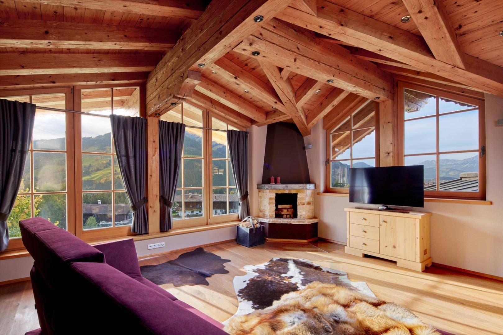 Gemütliches Wohnzimmer mit Holzbalkendecke, Kamin und weitem Bergblick durch große Fenster.