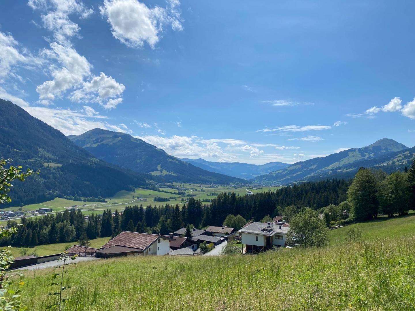 Idyllischer Ausblick über ein grünes Tal mit verstreuten Häusern und imposanten Bergen.