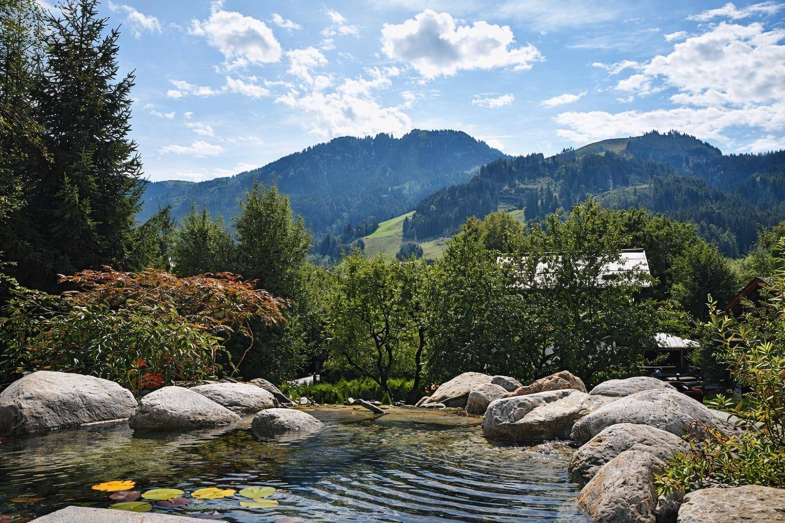 Malerischer Gartenteich mit Felsen und üppiger grüner Berglandschaft im Hintergrund.