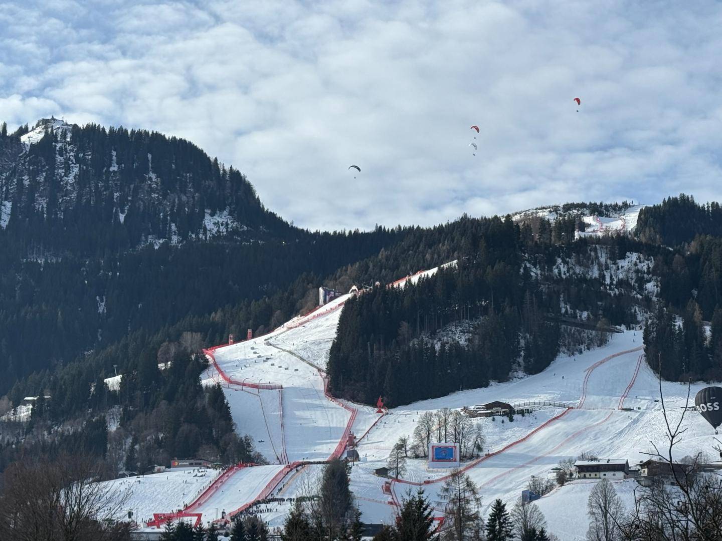 Beeindruckende Winterlandschaft mit verschneiten Skipisten und Paraglidern am Himmel.