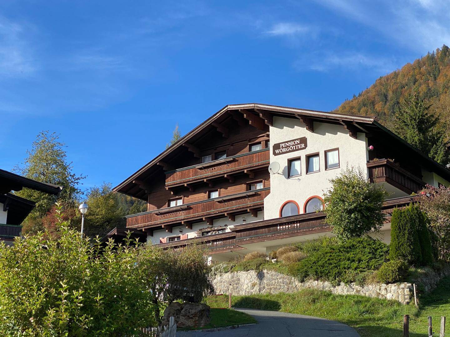 Alpines Gebäude mit Holzfassade und Balkonen, eingebettet in eine grüne Hügellandschaft.