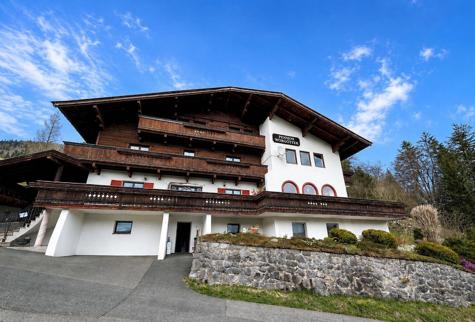 Traditionelles alpines Haus mit Holzbalkonen und Steinfundament unter blauem Himmel.