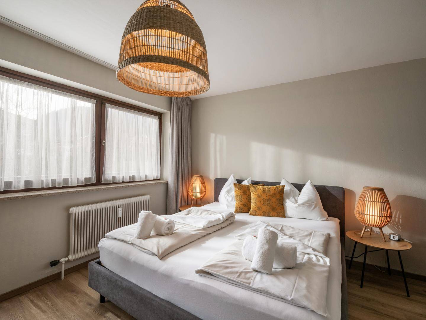 Helles Schlafzimmer mit Doppelbett, Holzboden und großen Fenstern, die viel Tageslicht hereinlassen.