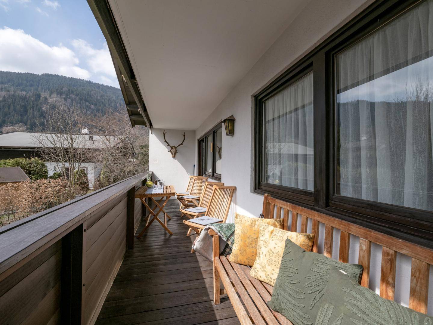 Geräumiger Balkon mit Holzboden, Sitzgelegenheiten und Blick auf die Berge und grüne Umgebung.