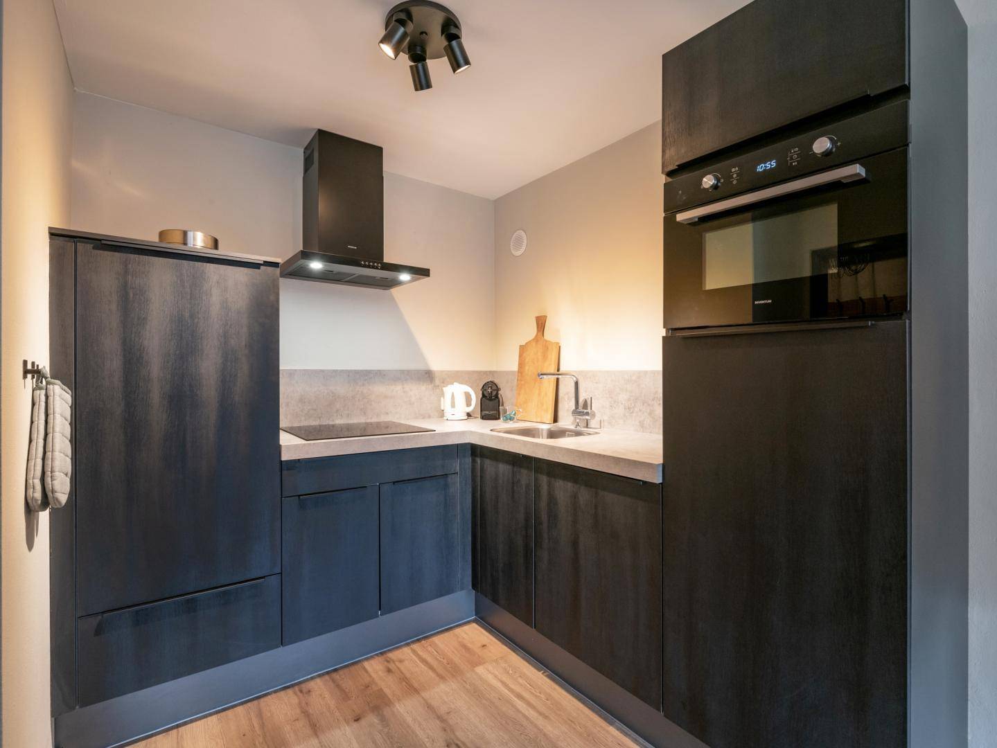 Moderne, kompakte Küche in dunklen Farbtönen mit integrierten Geräten und Dunstabzugshaube.
