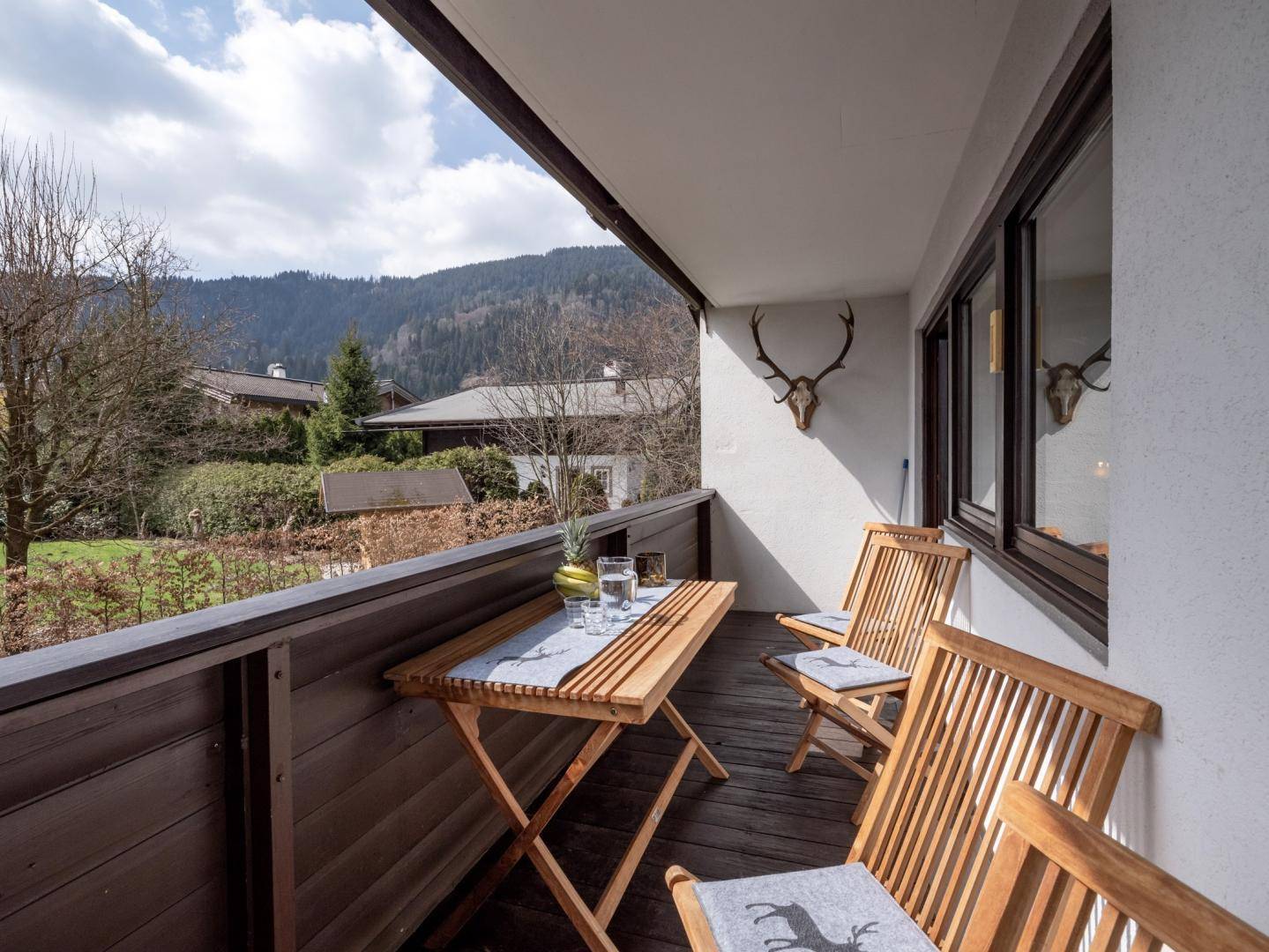 Sonniger Balkon mit Holztisch und Stühlen, ideal für Mahlzeiten im Freien mit Bergblick.
