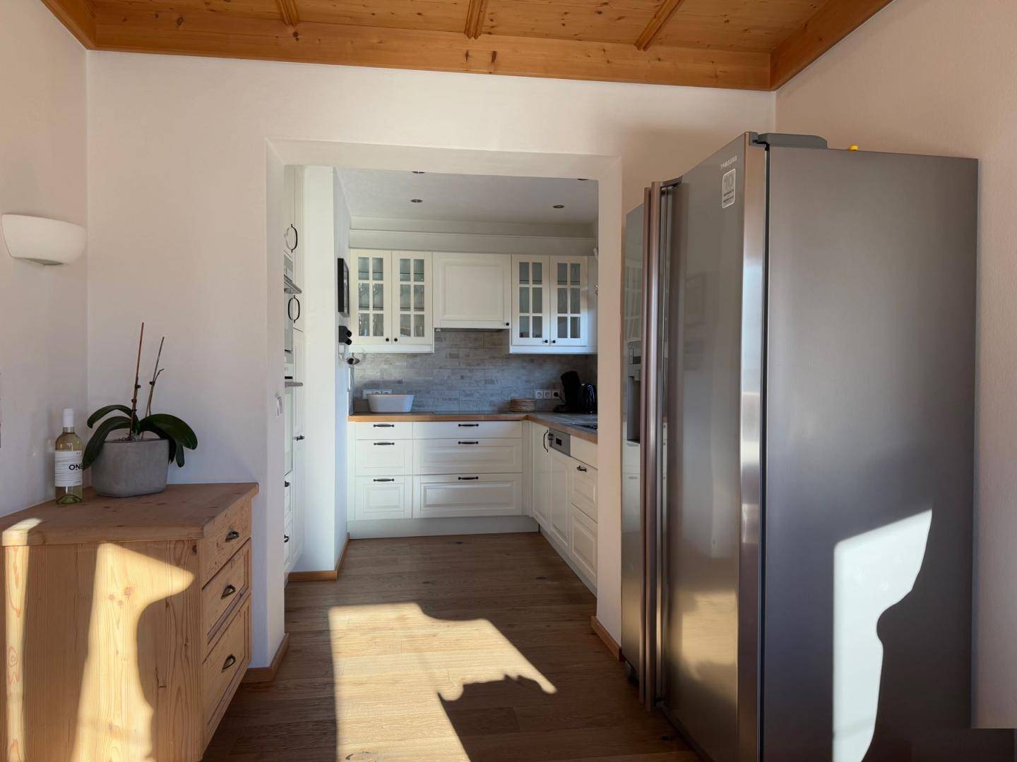 Eingangsbereich zur modernen Küche mit weißen Schränken und Edelstahlkühlschrank.