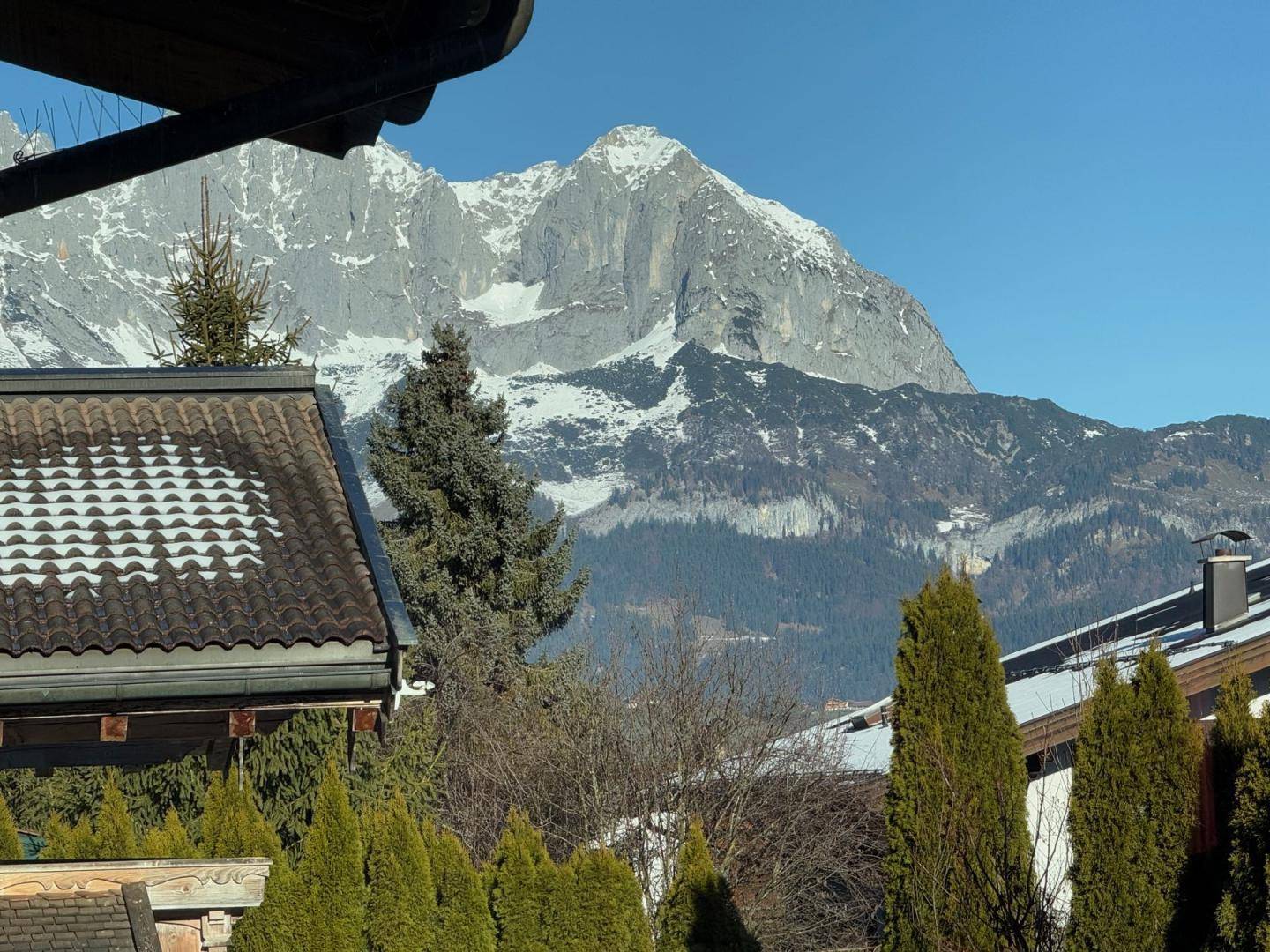 Beeindruckender Bergblick über Dächer und Bäume an einem sonnigen Tag.
