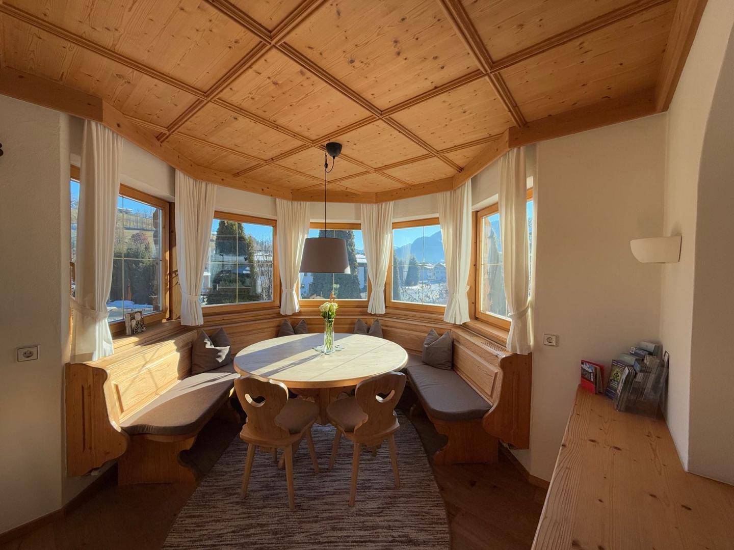 Heller Essbereich mit Holztäfelung, Eckbank und vielen Fenstern mit Ausblick.