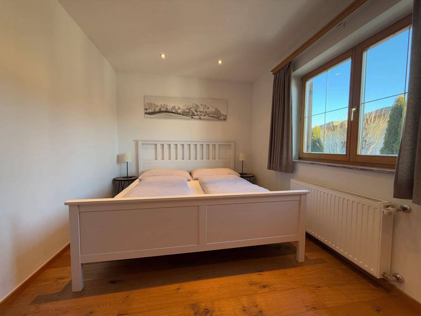 Helles Schlafzimmer mit Doppelbett, Holzboden und großem Fenster.