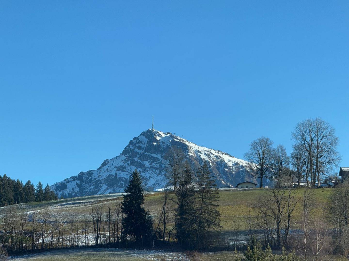 Majestätischer Berg mit Sendemast, umgeben von grünen Wiesen und Bäumen.