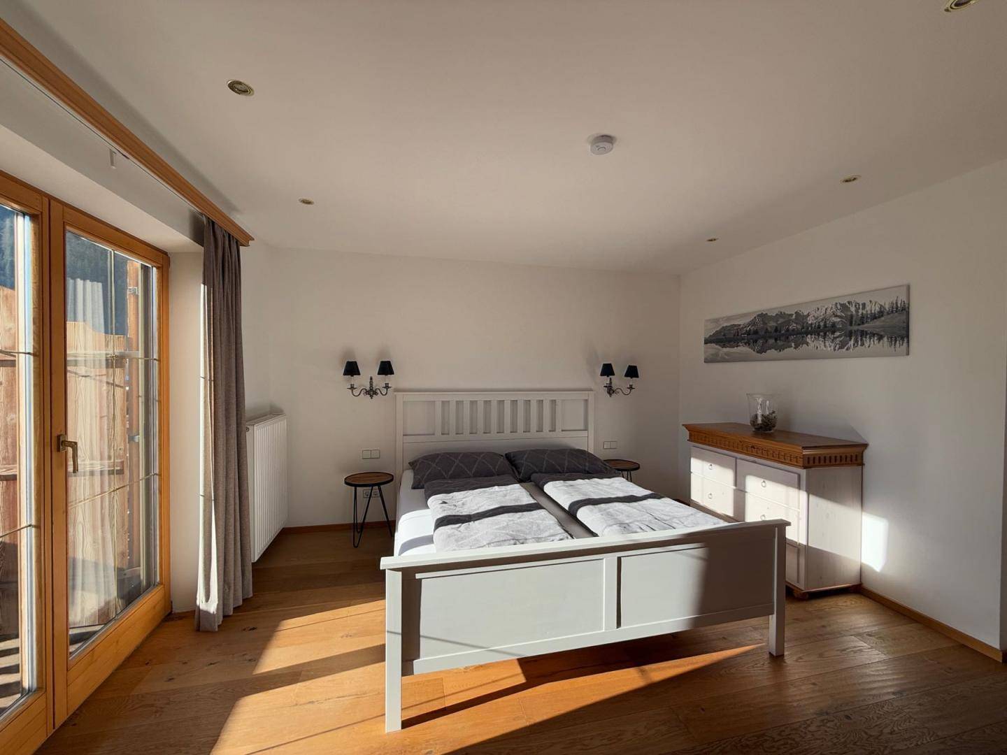 Helles Schlafzimmer mit Doppelbett, Holzboden und Zugang zu einem Balkon.