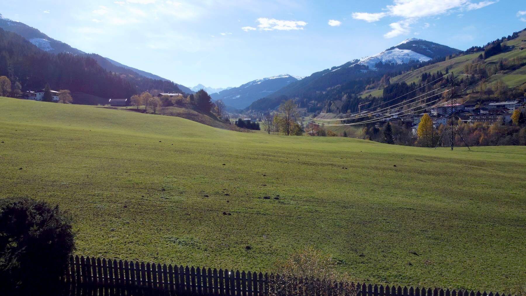 Weitläufiger Blick über grüne Felder auf schneebedeckte Berge und ein malerisches Dorf.