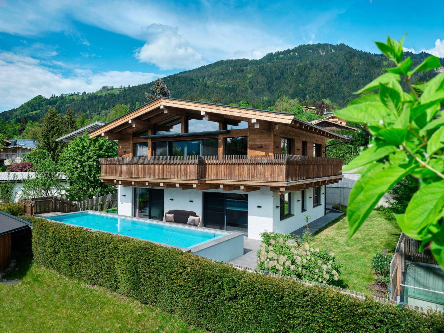 Moderne Villa mit Außenpool, Holzfassade und Bergblick in grüner Umgebung.