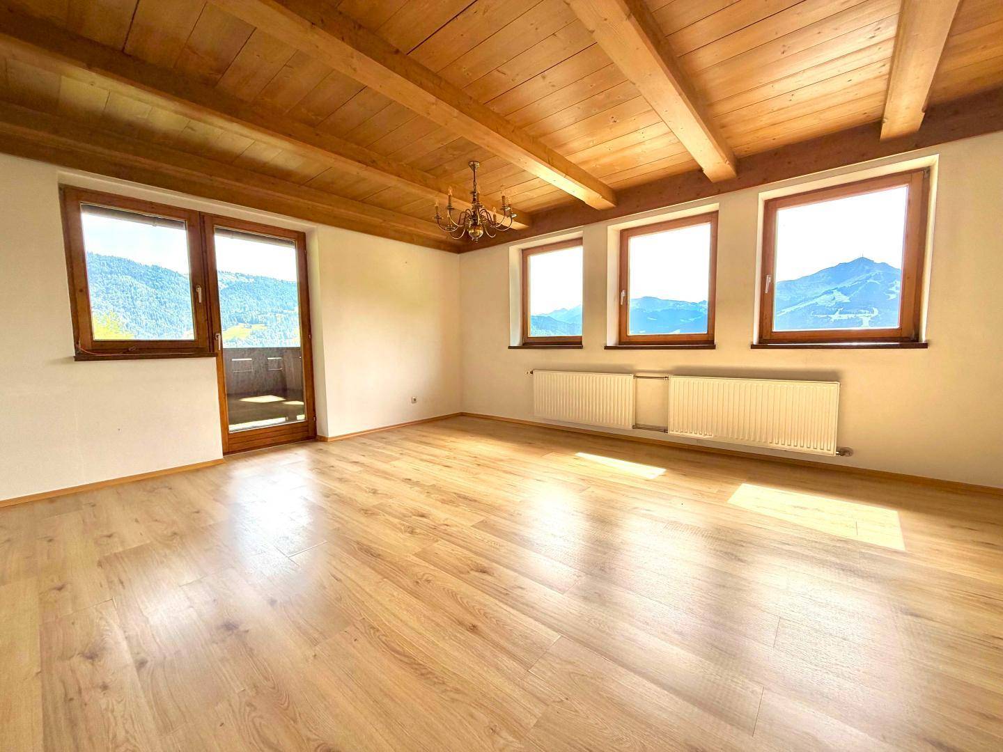 Heller Raum mit Holzboden, sichtbaren Deckenbalken und Bergblick durch große Fenster.