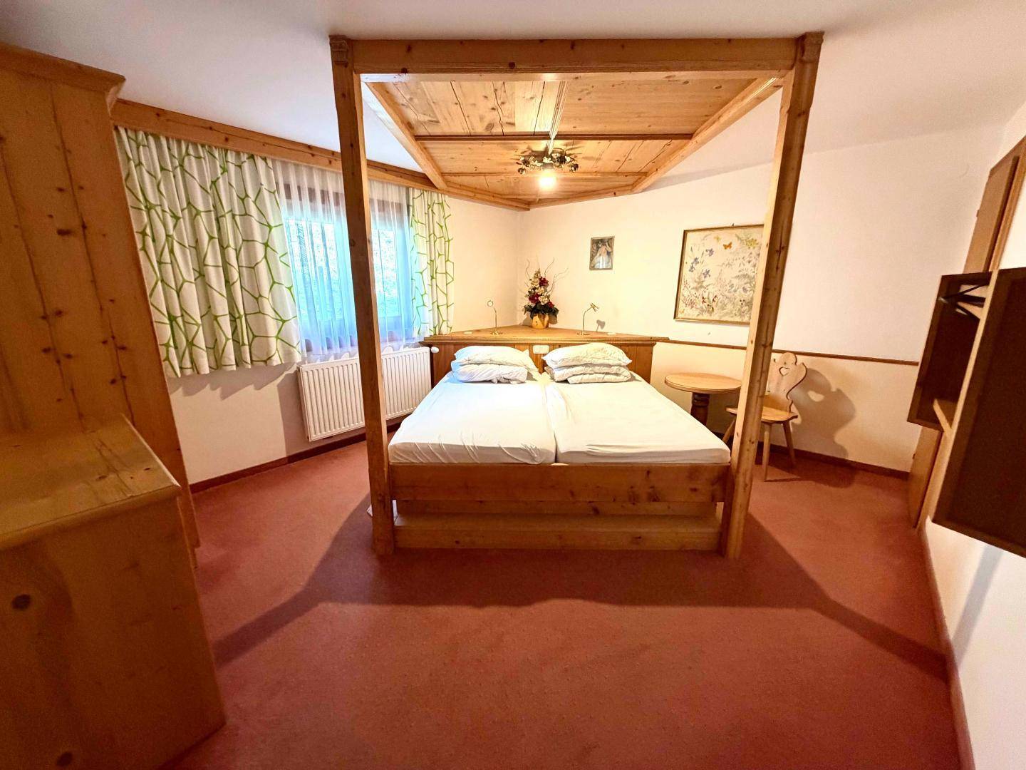 Gemütliches Schlafzimmer mit Himmelbett aus Holz, rotem Teppichboden und Einbauschränken.
