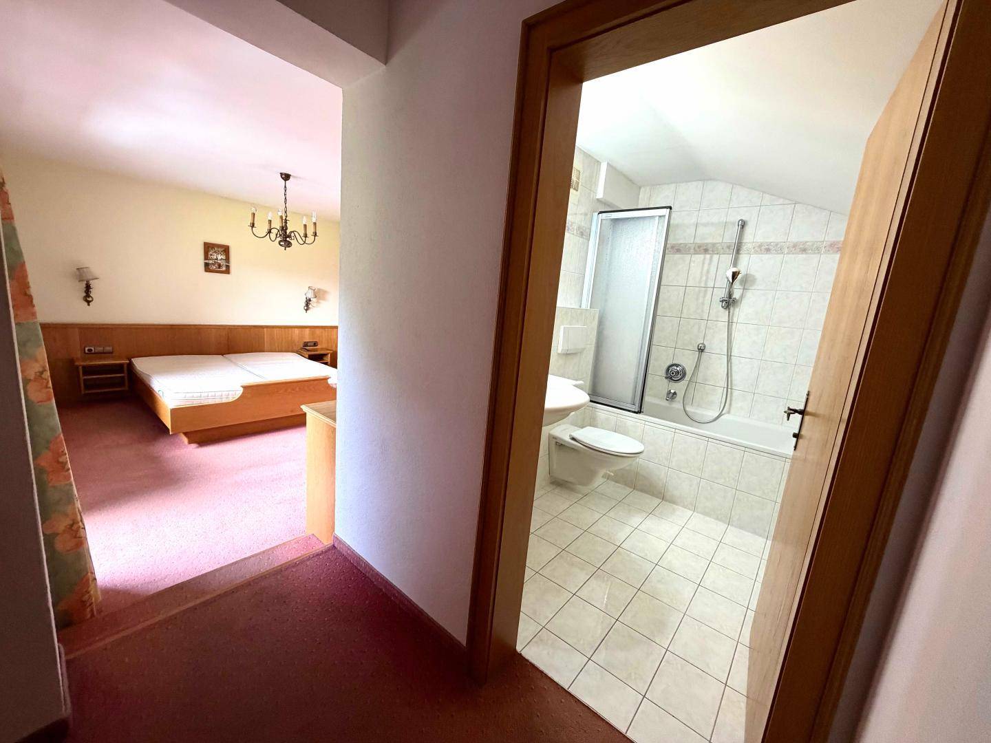 Flur mit Blick in ein Schlafzimmer und ein Badezimmer mit Dusche und Badewanne.