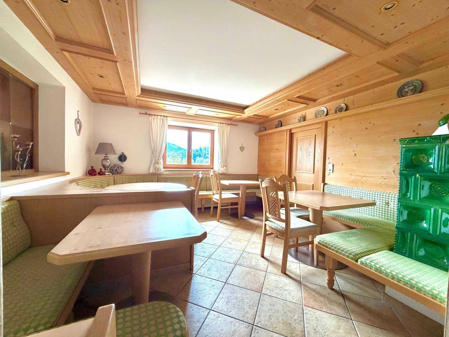 Gemütlicher Essbereich im alpenländischen Stil mit Holztäfelung, Kachelofen und karierten Sitzbänken.