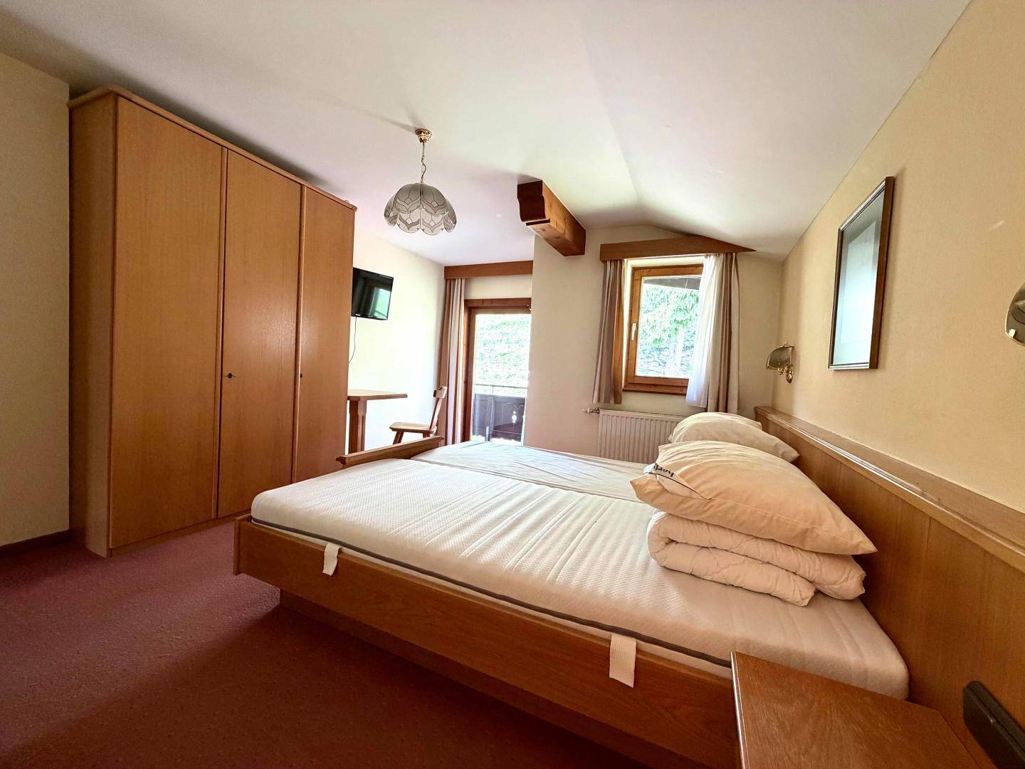Helles Schlafzimmer mit zwei Einzelbetten, Holzschrank und Zugang zu einem Balkon.