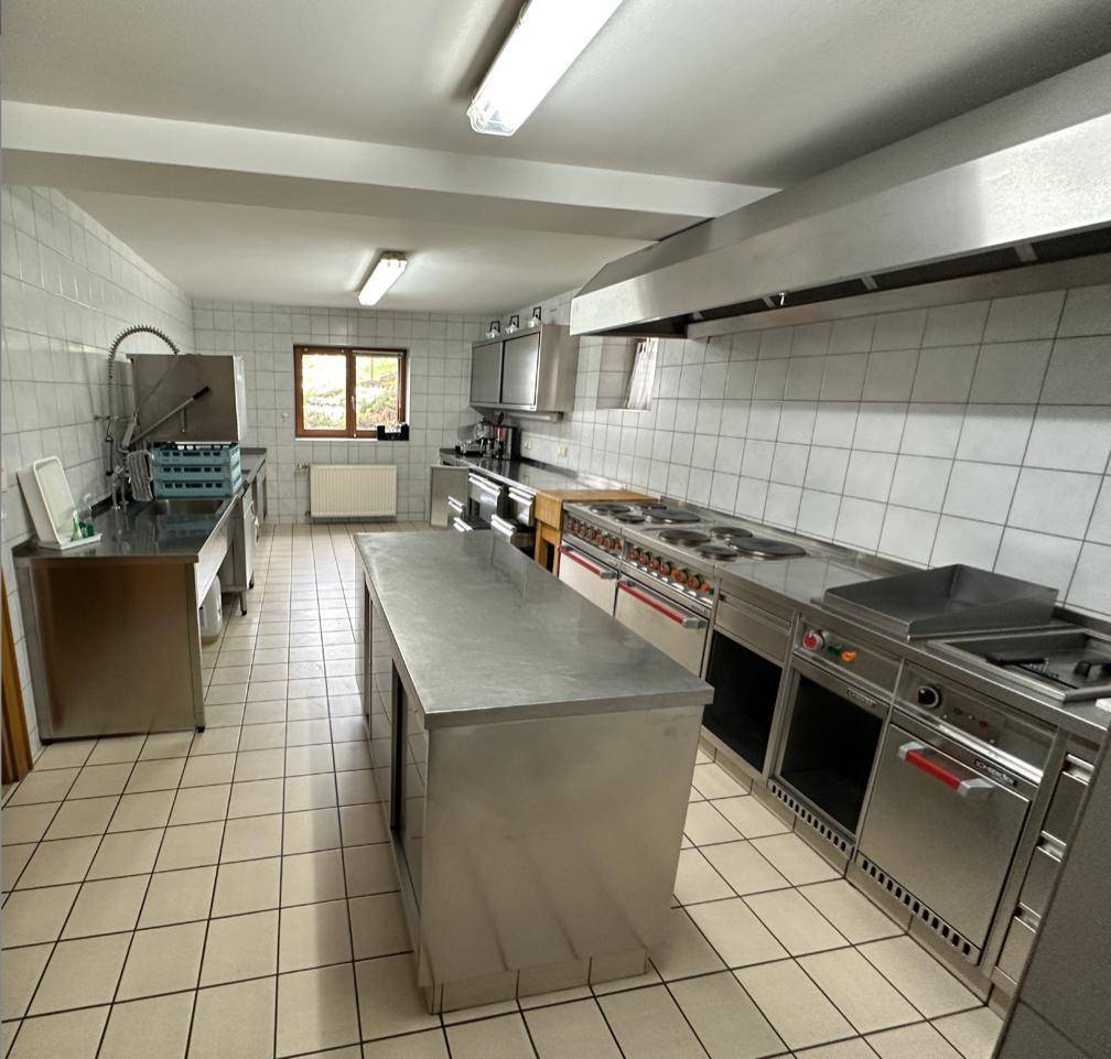 Professionelle Küche mit umfangreicher Edelstahlausstattung, Fliesenboden und großem Dunstabzug.