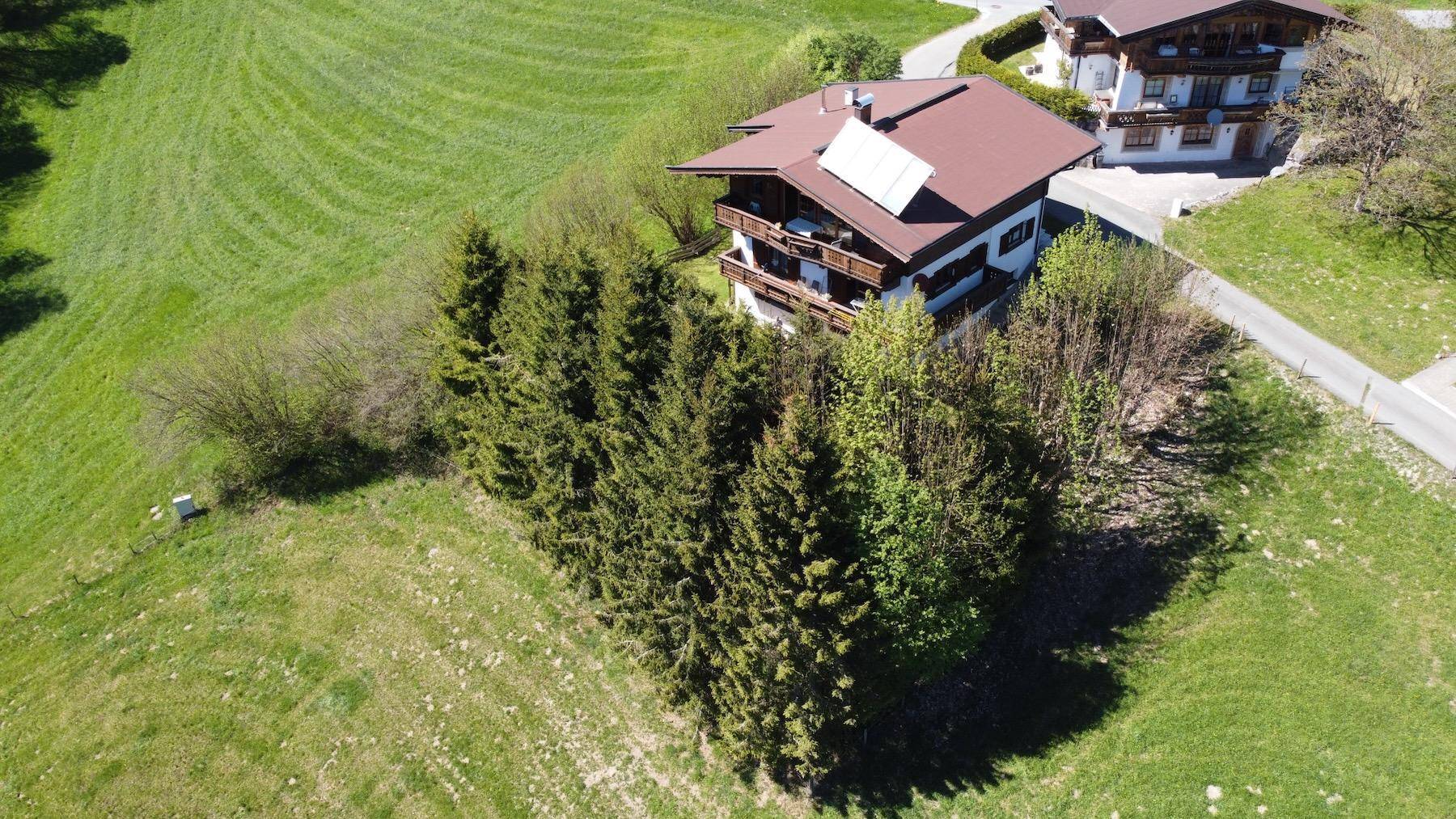 Luftaufnahme eines Alpenhauses mit Solaranlage, umgeben von Nadelbäumen und grünen Wiesen in alpiner Landschaft.