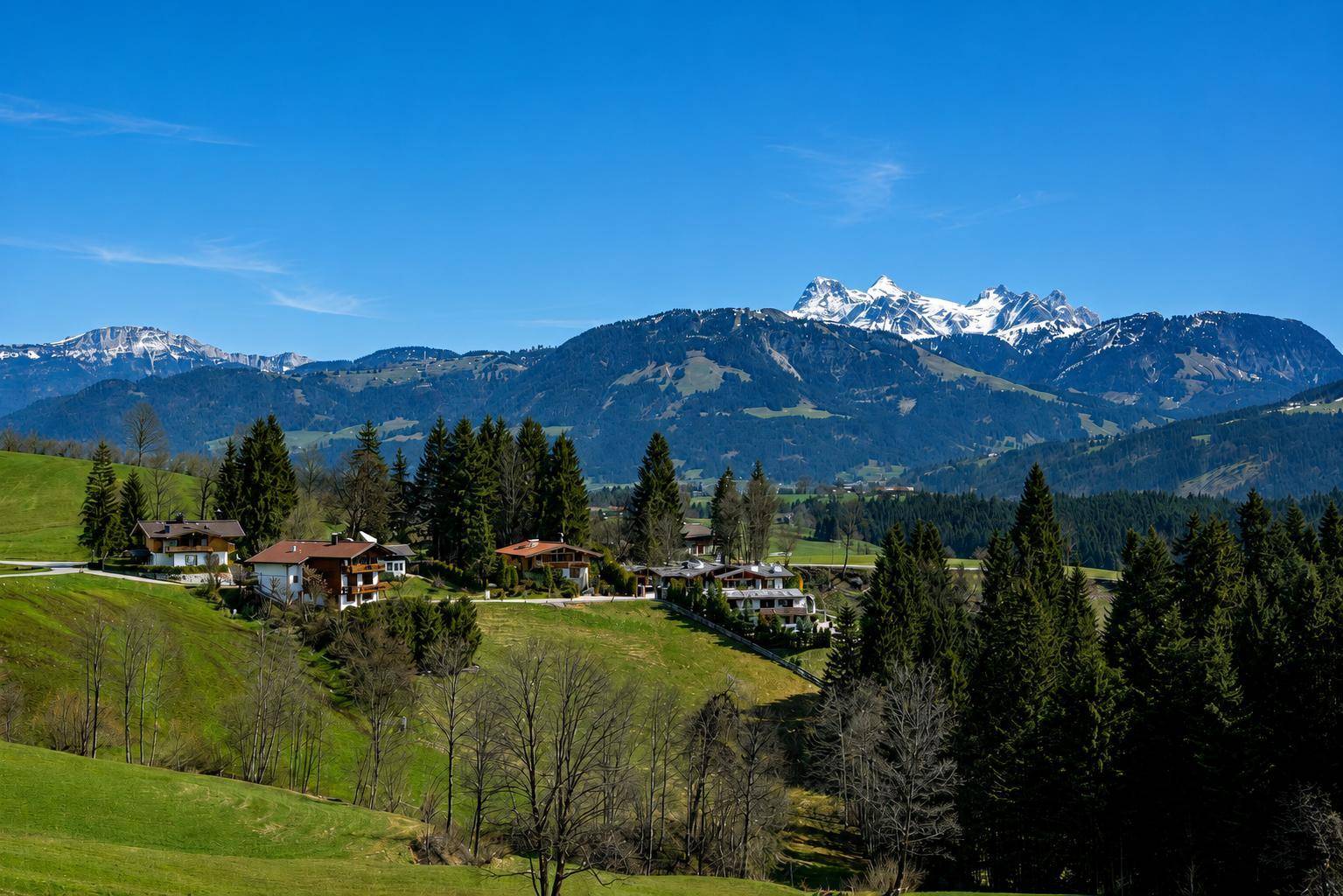 Malerisches Dorf in den grünen Hügeln der Alpen, umgeben von Wäldern und majestätischen Berggipfeln.