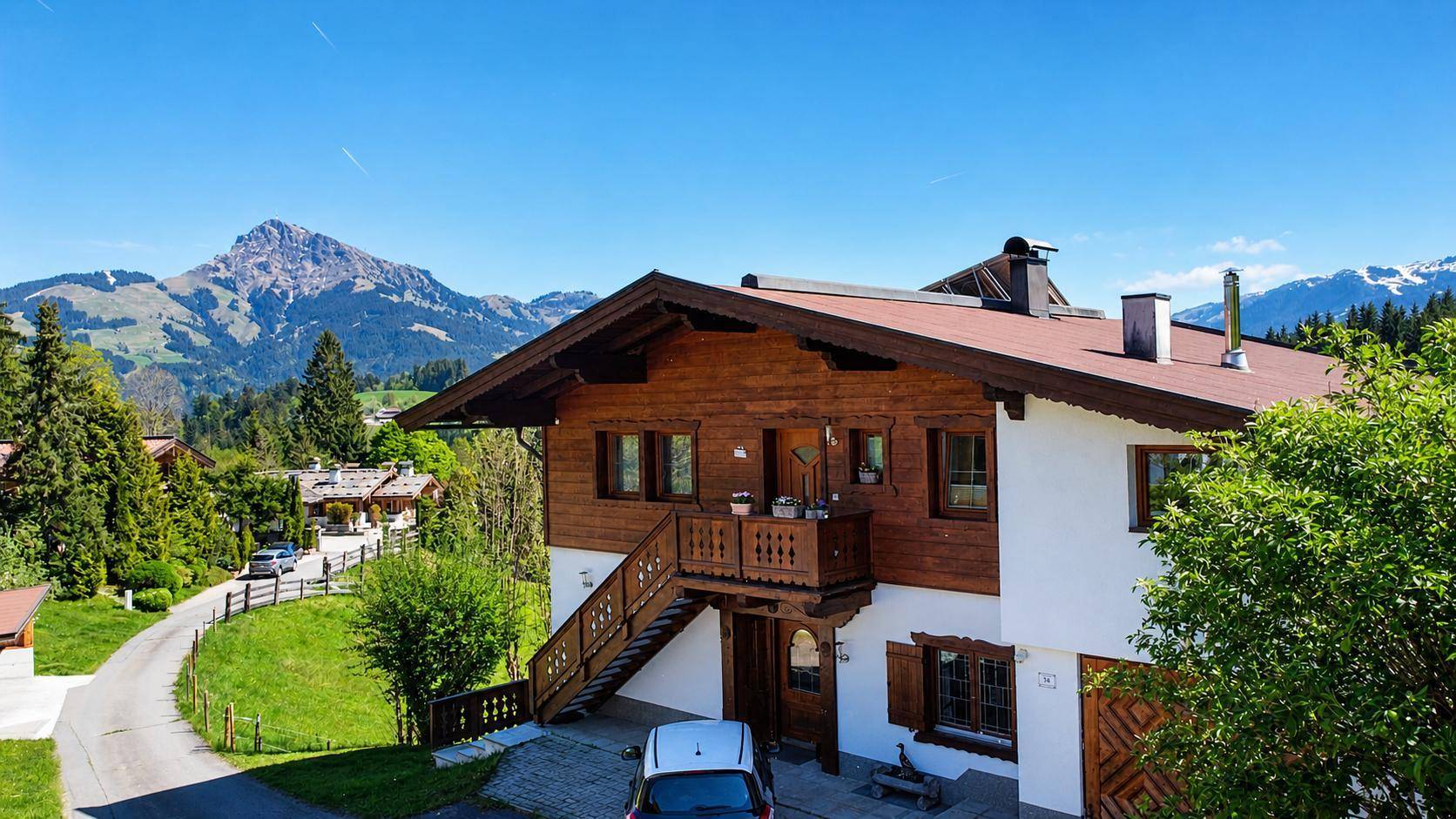 Charmantes Alpenhaus mit Holzbalkonen und Außentreppe, umgeben von grüner Natur und Bergblick.