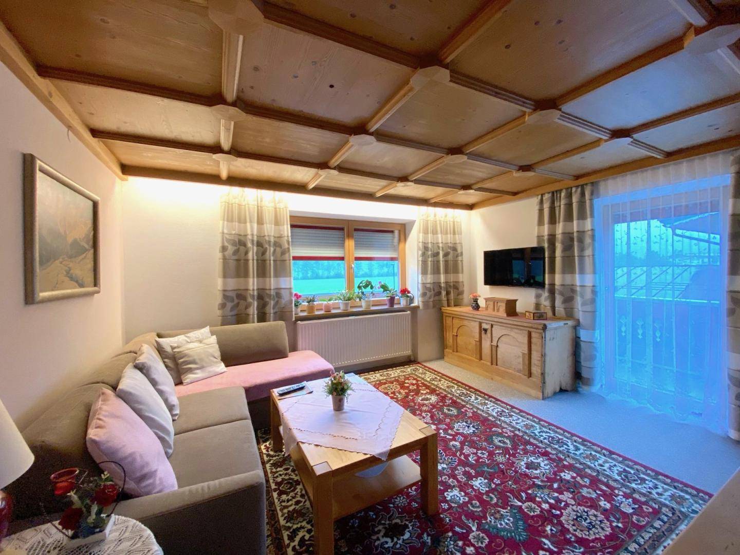Gemütliches Wohnzimmer im Landhausstil mit Holzpaneeldecke, Teppich und bequemer Sitzecke.