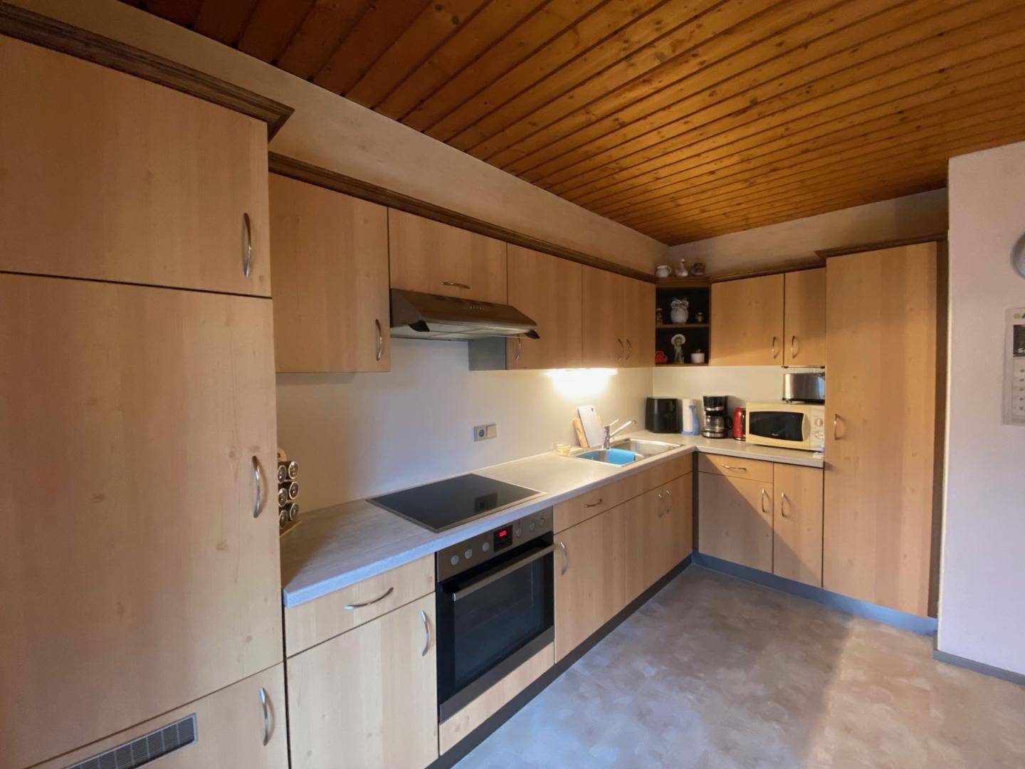 Funktionale Küche mit hellen Holzschränken, Einbaugeräten und Holzpaneeldecke.