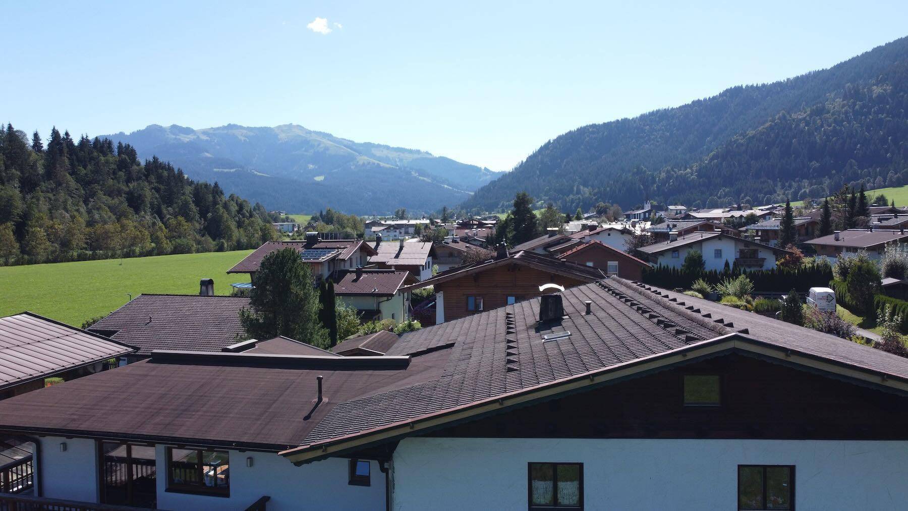 Panoramablick über die Dächer des Dorfes und die umliegende Berglandschaft unter blauem Himmel.