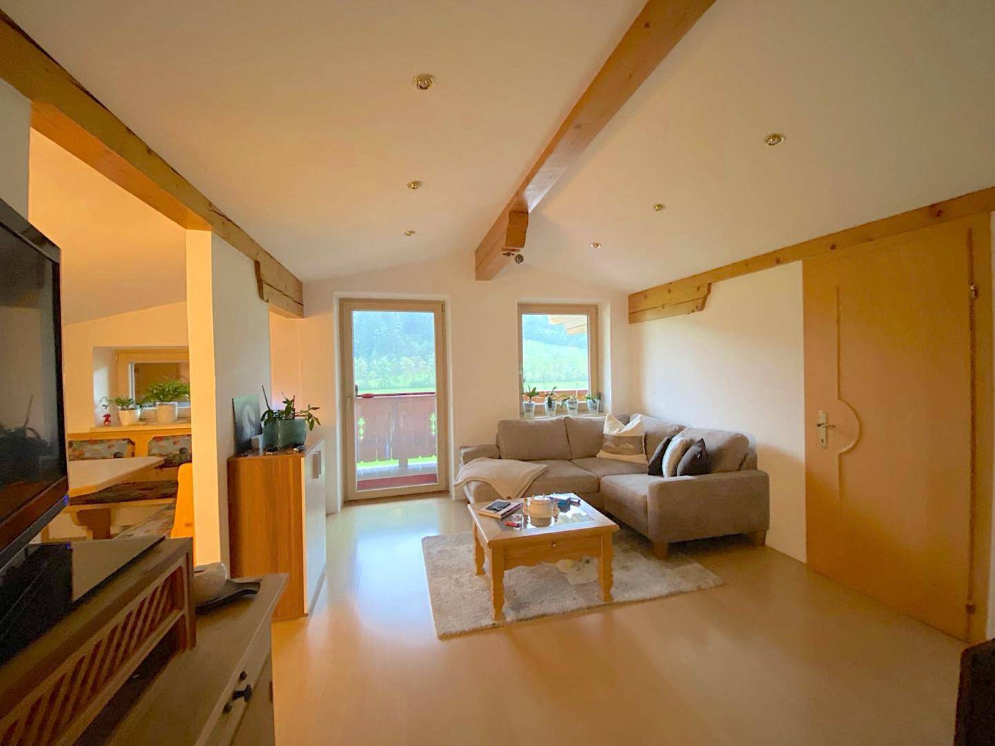 Helles Wohnzimmer mit Holzbalken, bequemer Couch und Zugang zu einem Balkon.