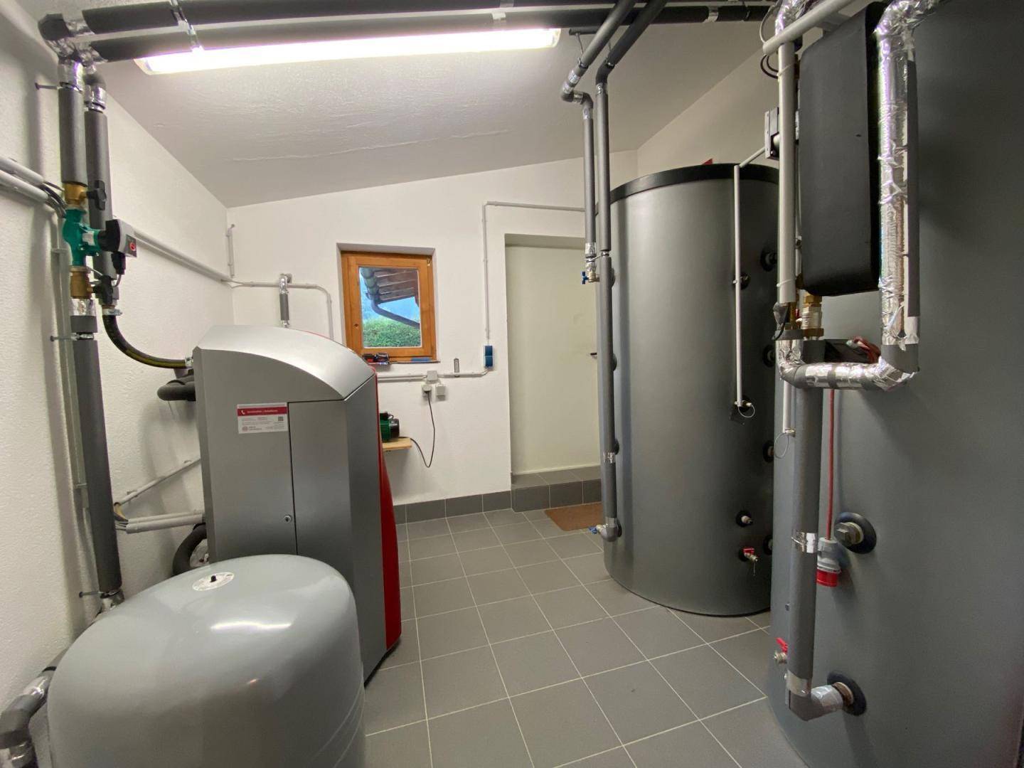 Technikraum mit Heizungsanlage, Warmwasserspeichern und gefliestem Boden.