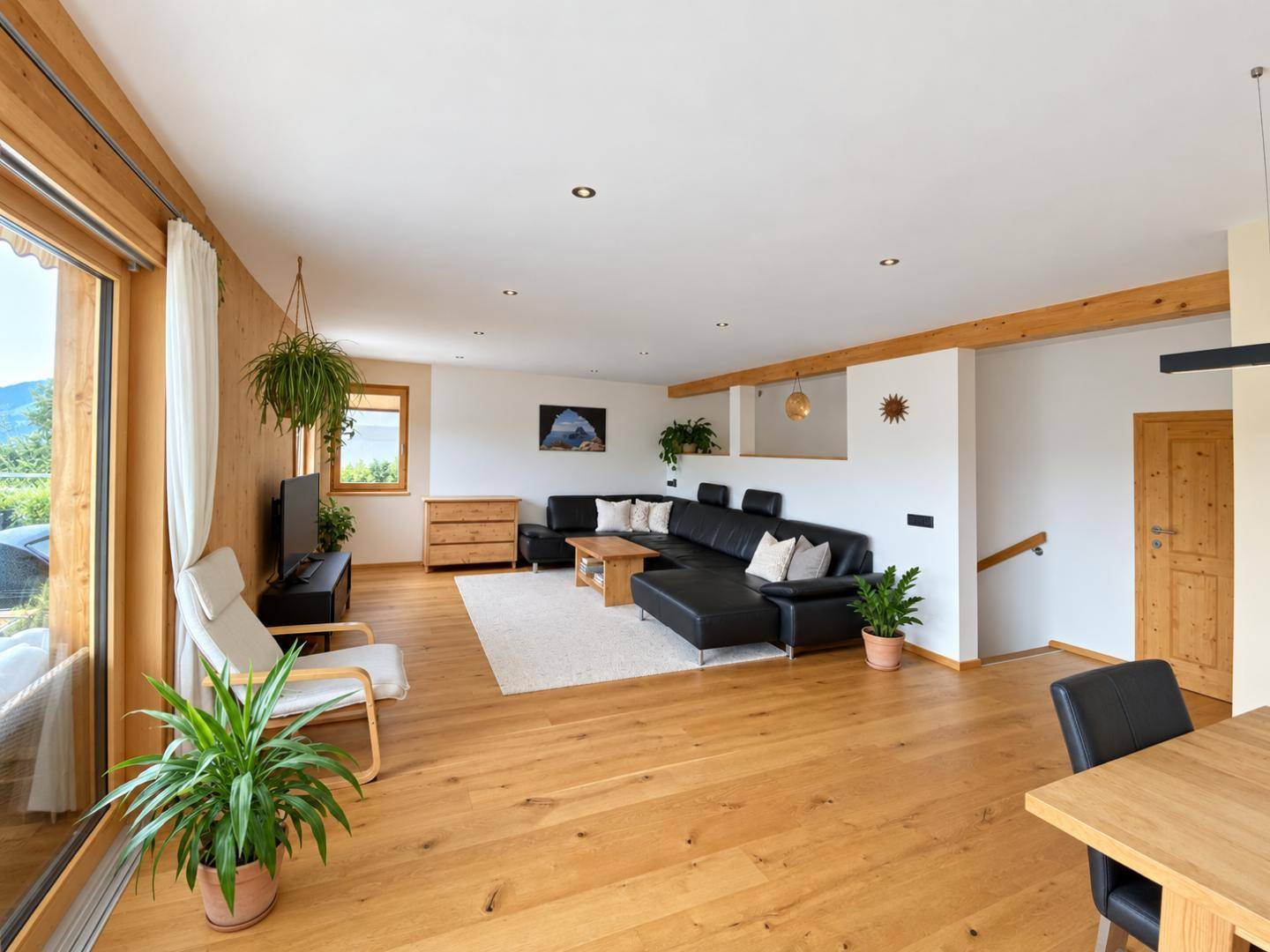 Helles Wohnzimmer mit Eichenparkett, großem Sofa und bodentiefen Fenstern mit Bergblick.