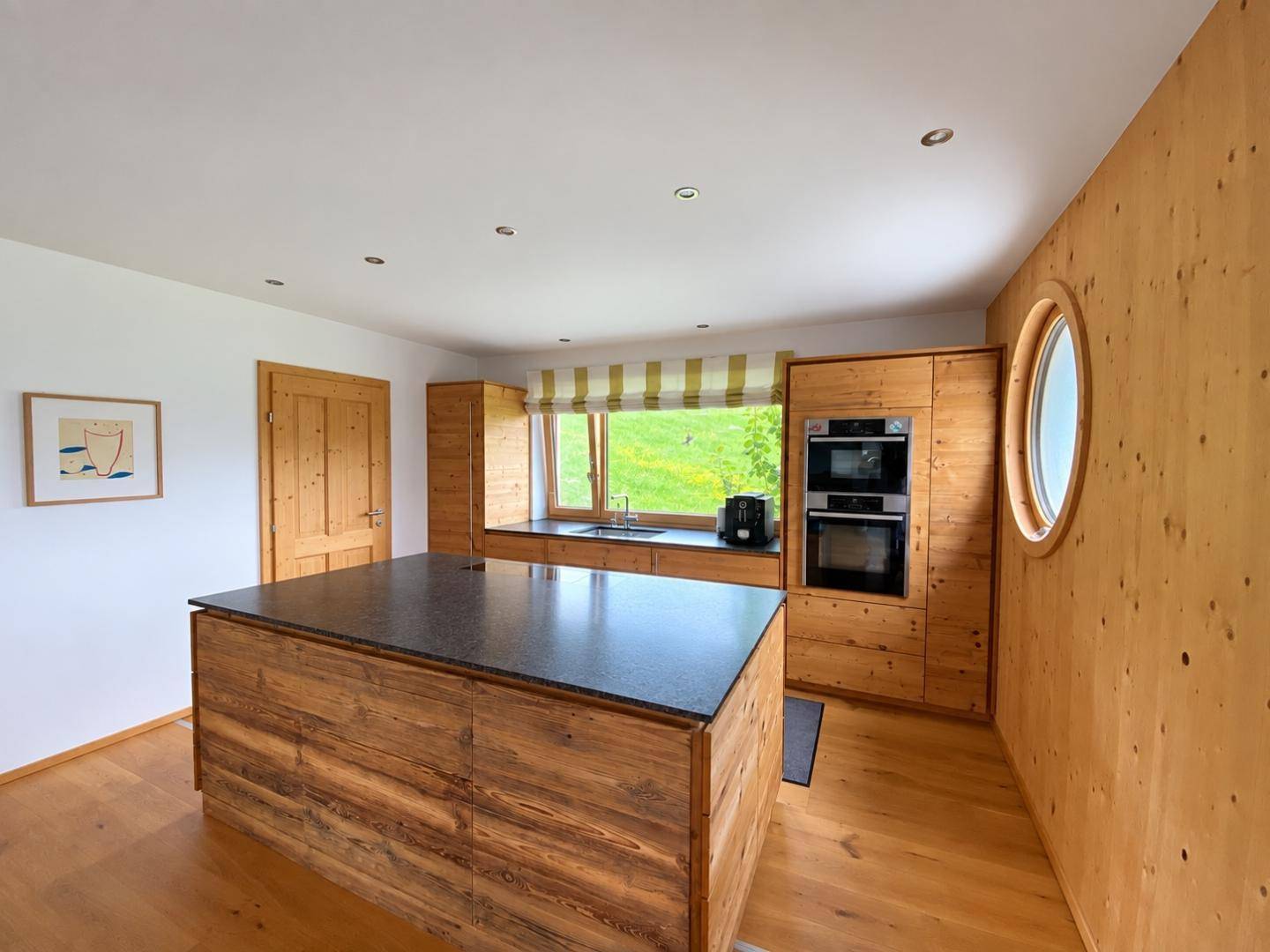 Moderne Holzküche mit Kücheninsel, integrierten Geräten und einem runden Fenster.