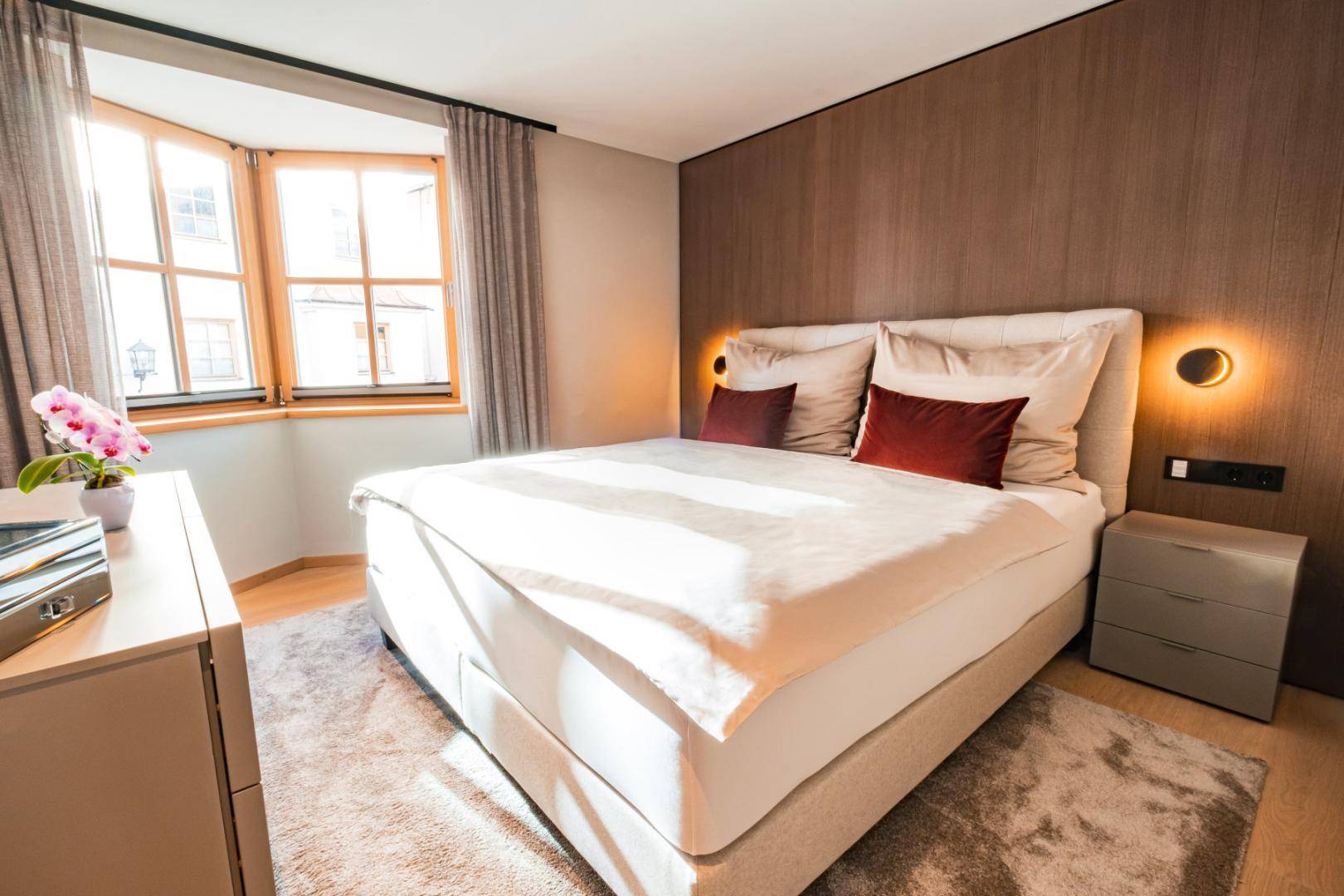 Helles Schlafzimmer mit Erkerfenster, Doppelbett und Holzboden, durchflutet von Sonnenlicht.