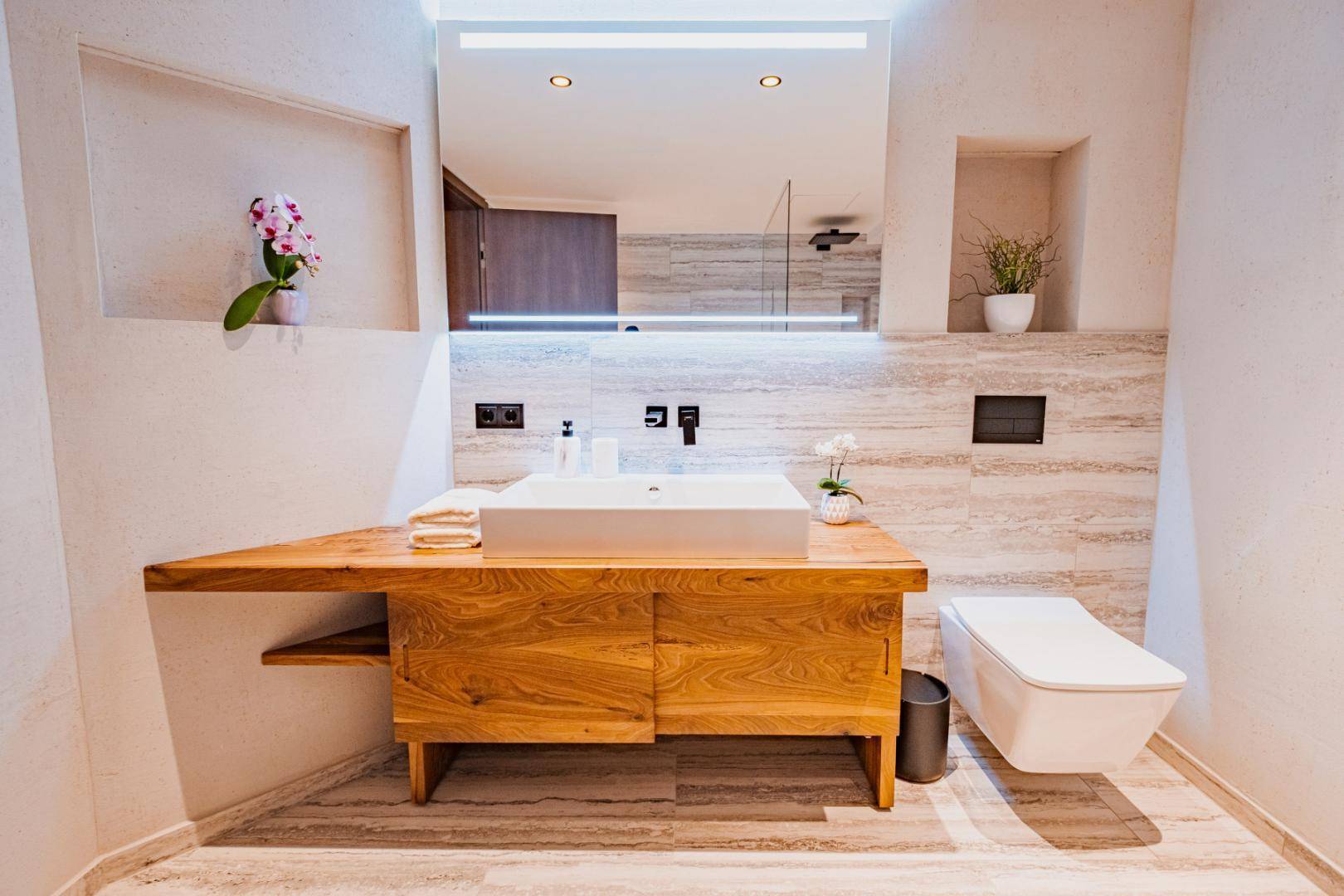 Elegantes Badezimmer mit Holzwaschtisch, Wand-WC und großem beleuchteten Spiegel.