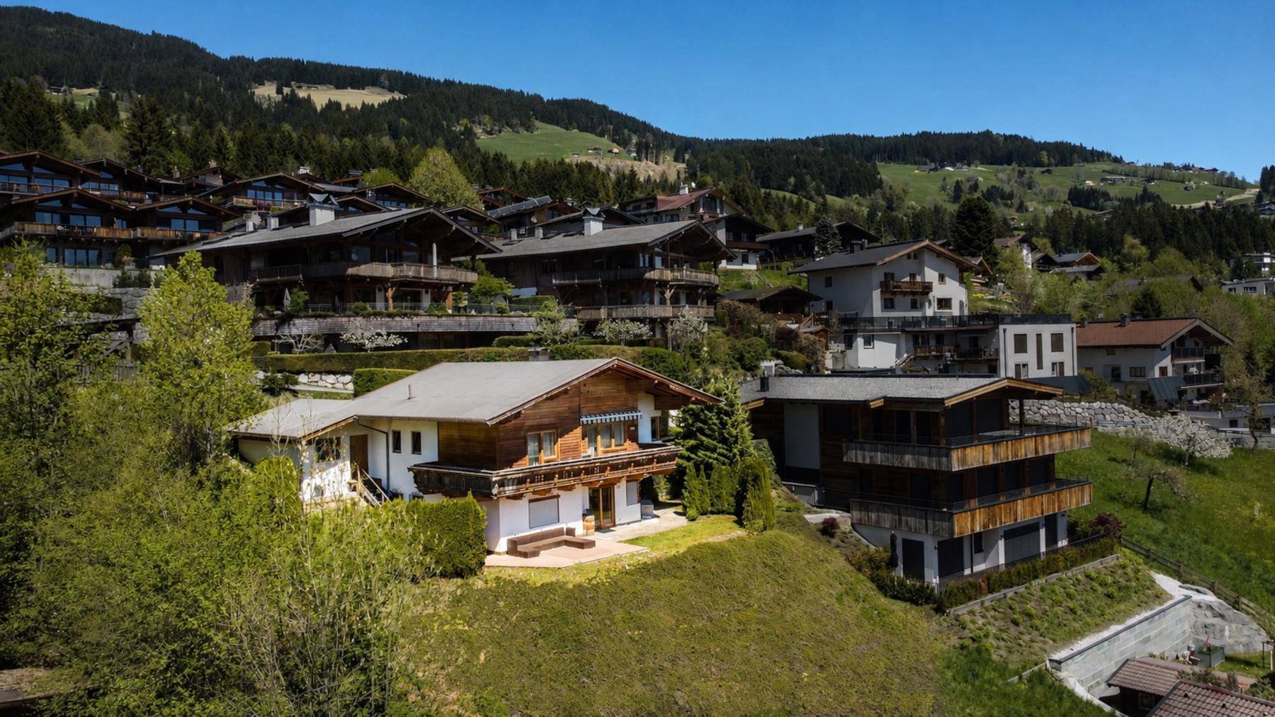 Idyllische Berglandschaft mit mehreren Chalets und üppiger Vegetation unter blauem Himmel.