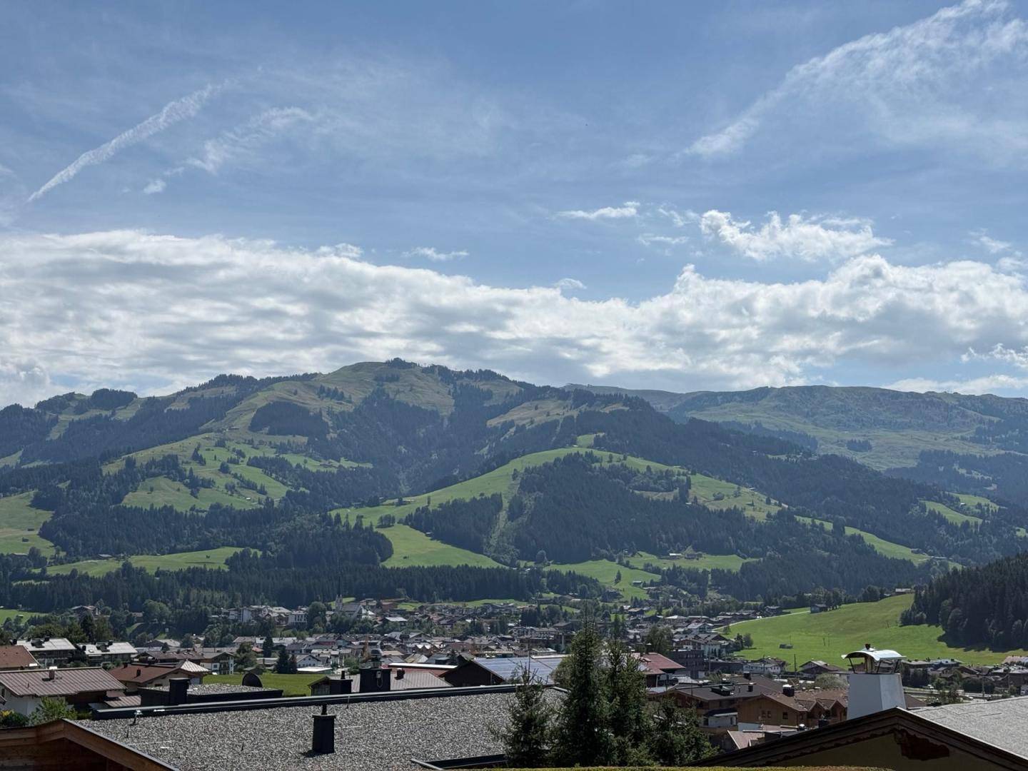 Weitläufiger Panoramablick über ein grünes Tal mit Bergen und einer Siedlung im Sonnenschein.