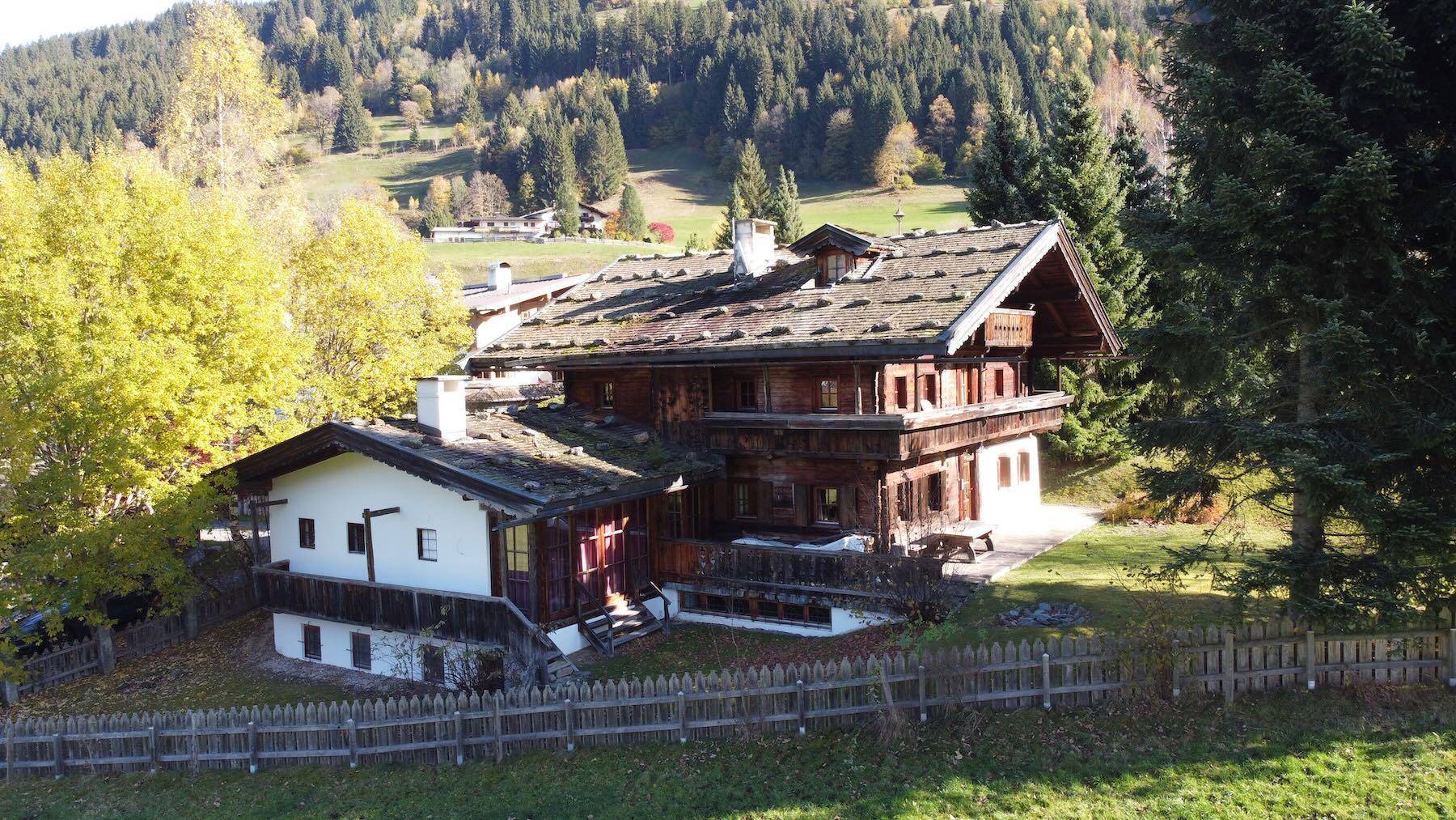 Charmantes alpines Anwesen mit mehreren Gebäudeteilen, Holzbalkonen und umzäuntem Gartenbereich in ländlicher Umgebung.